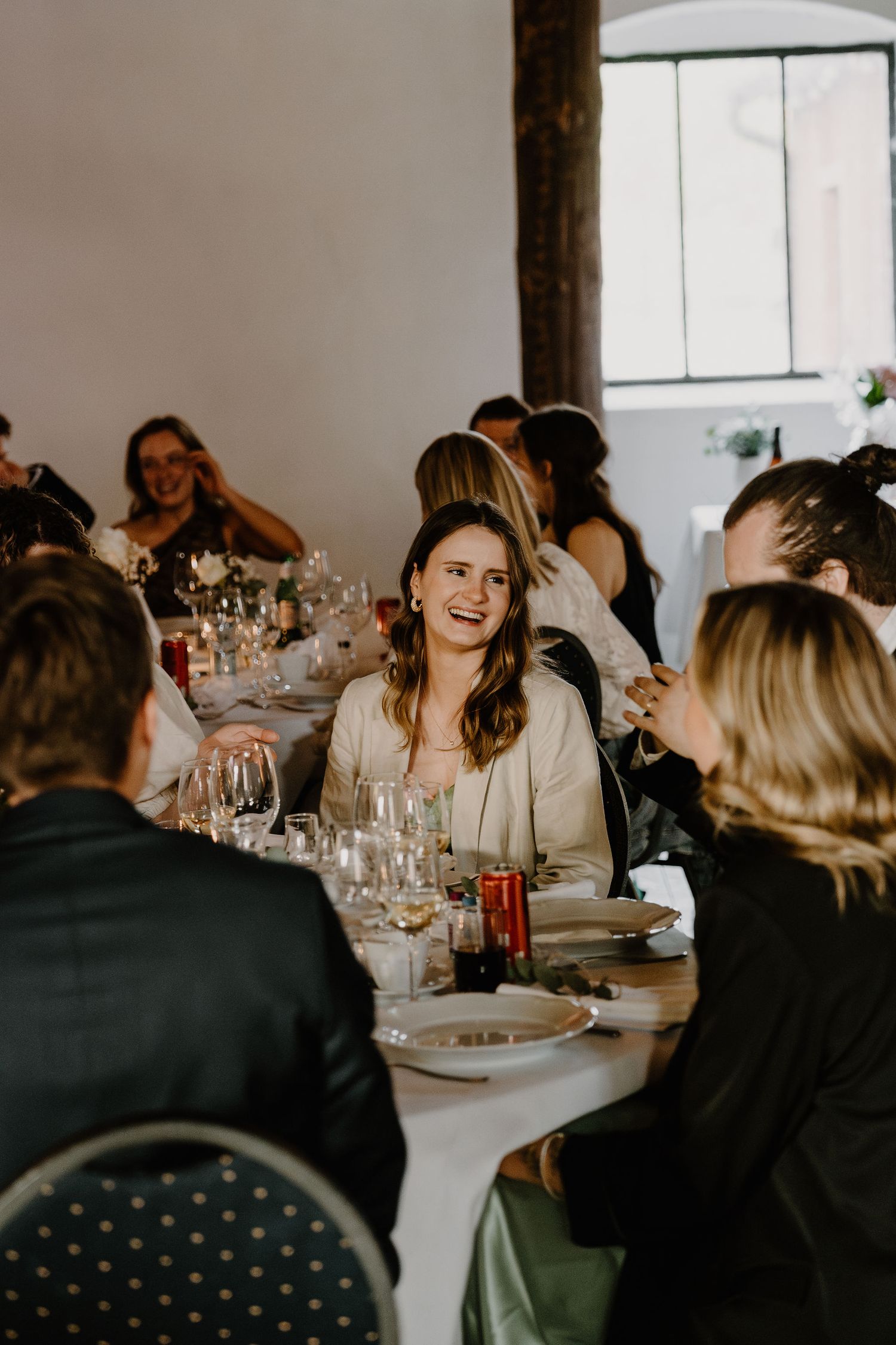 People enjoying a festive gathering at a long dining table with wine glasses and table settings in a bright indoor space.