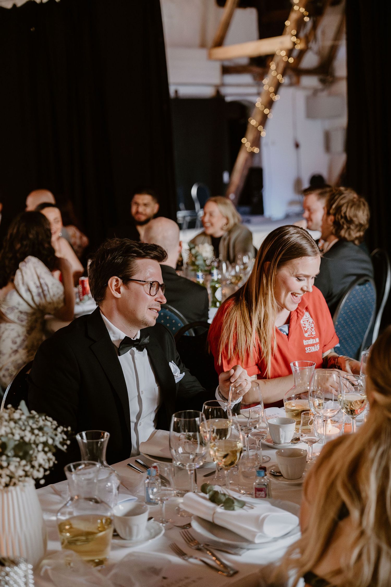 Wedding reception guests sit at elegantly decorated tables with candlelight and white floral centerpieces.