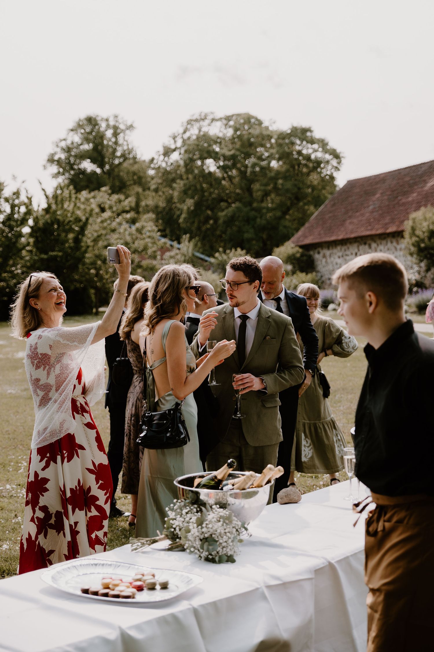 Wedding reception guests gathered around tables with white linens at an outdoor celebration in elegant afternoon setting.