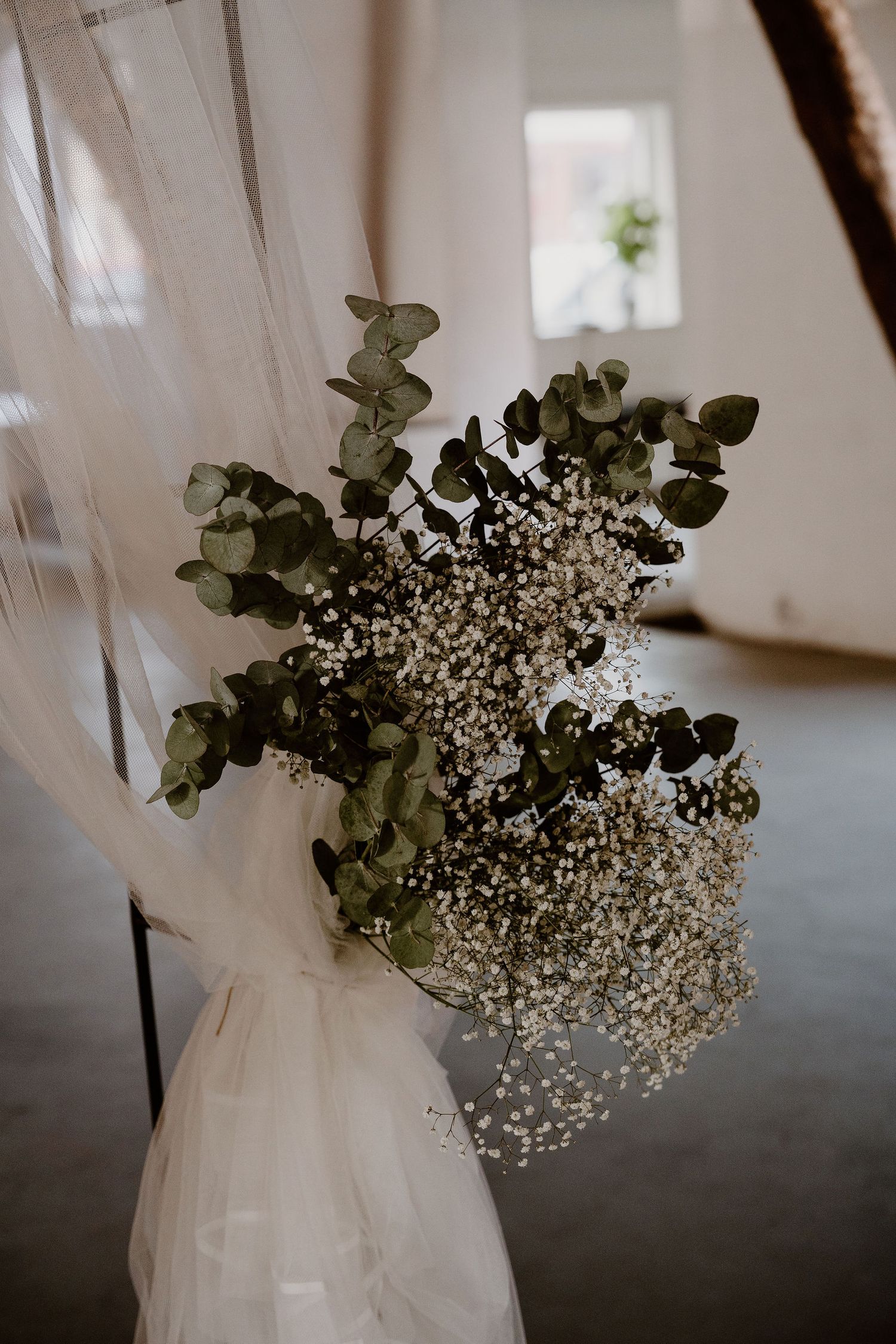 White curtains gently frame a delicate arrangement of baby's breath and eucalyptus against natural light.
