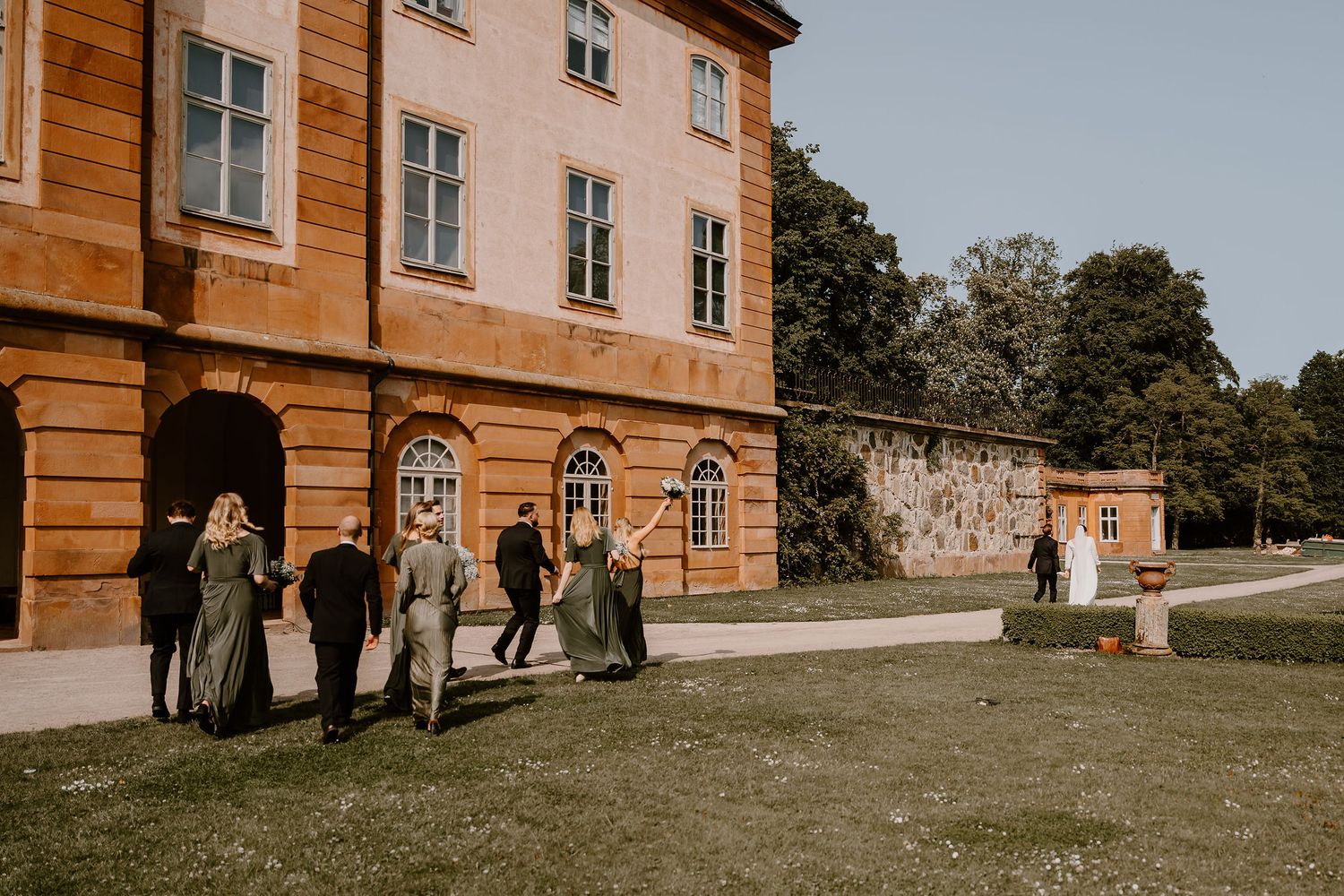 Traditional terracotta-colored manor house with multiple windows and guests gathered outside during an event.