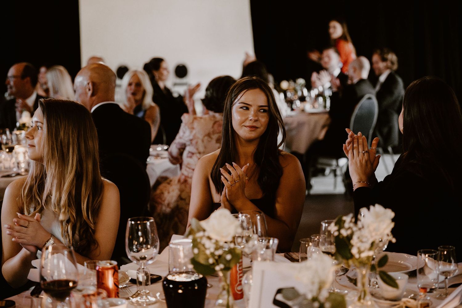 Wedding reception guests seated at an elegant table with wine glasses and floral centerpieces during an evening celebration.