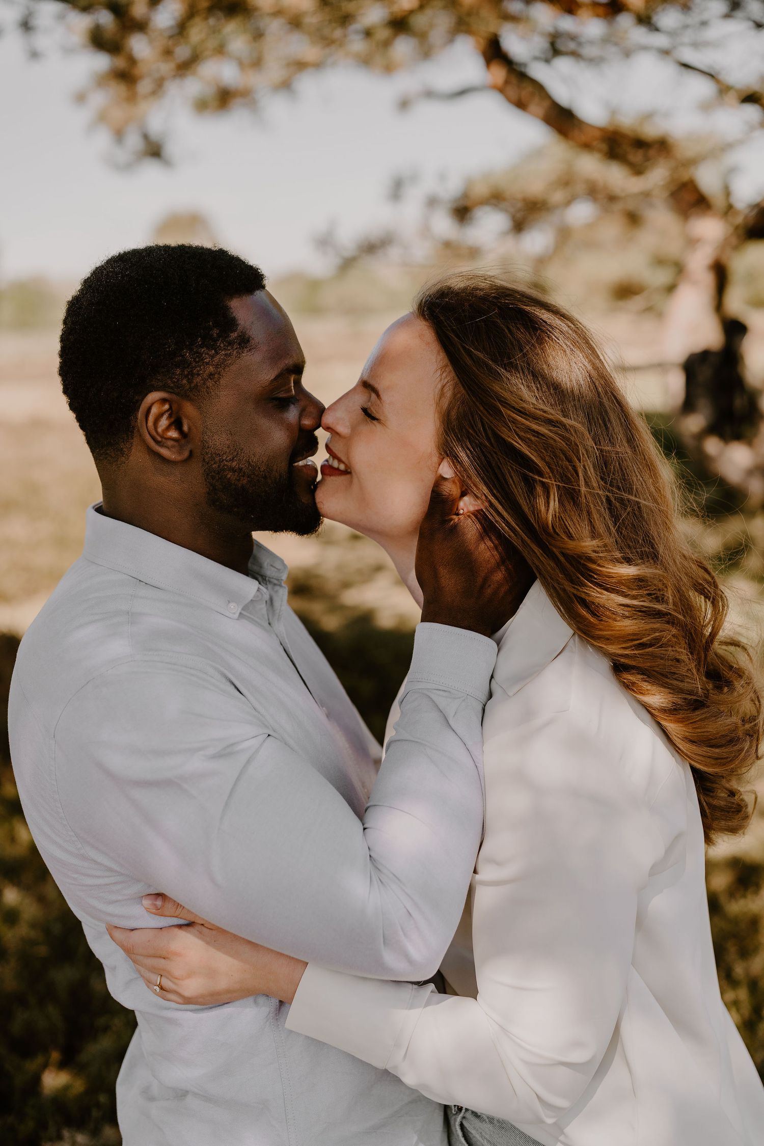 A couple in matching white outfits sharing an intimate moment outdoors during a romantic photoshoot.