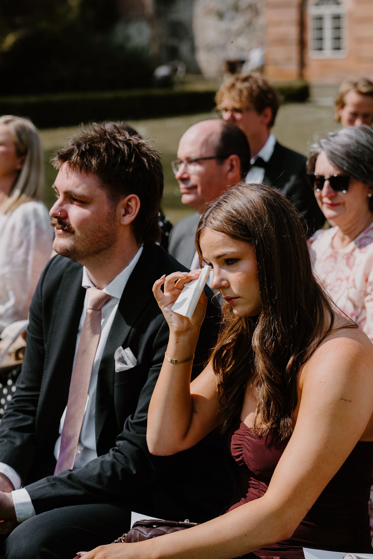Wedding guests sitting in rows at an outdoor ceremony show emotional reactions during a special moment.