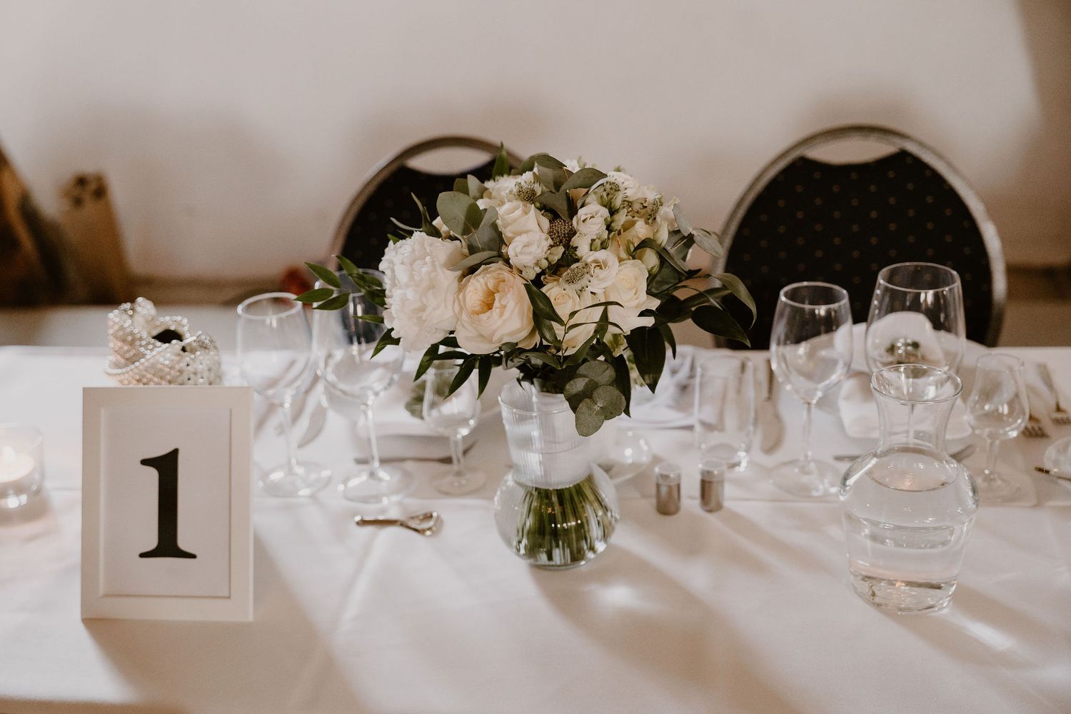 Elegant wedding reception tables adorned with white floral centerpieces and place settings in a neutral-toned venue.