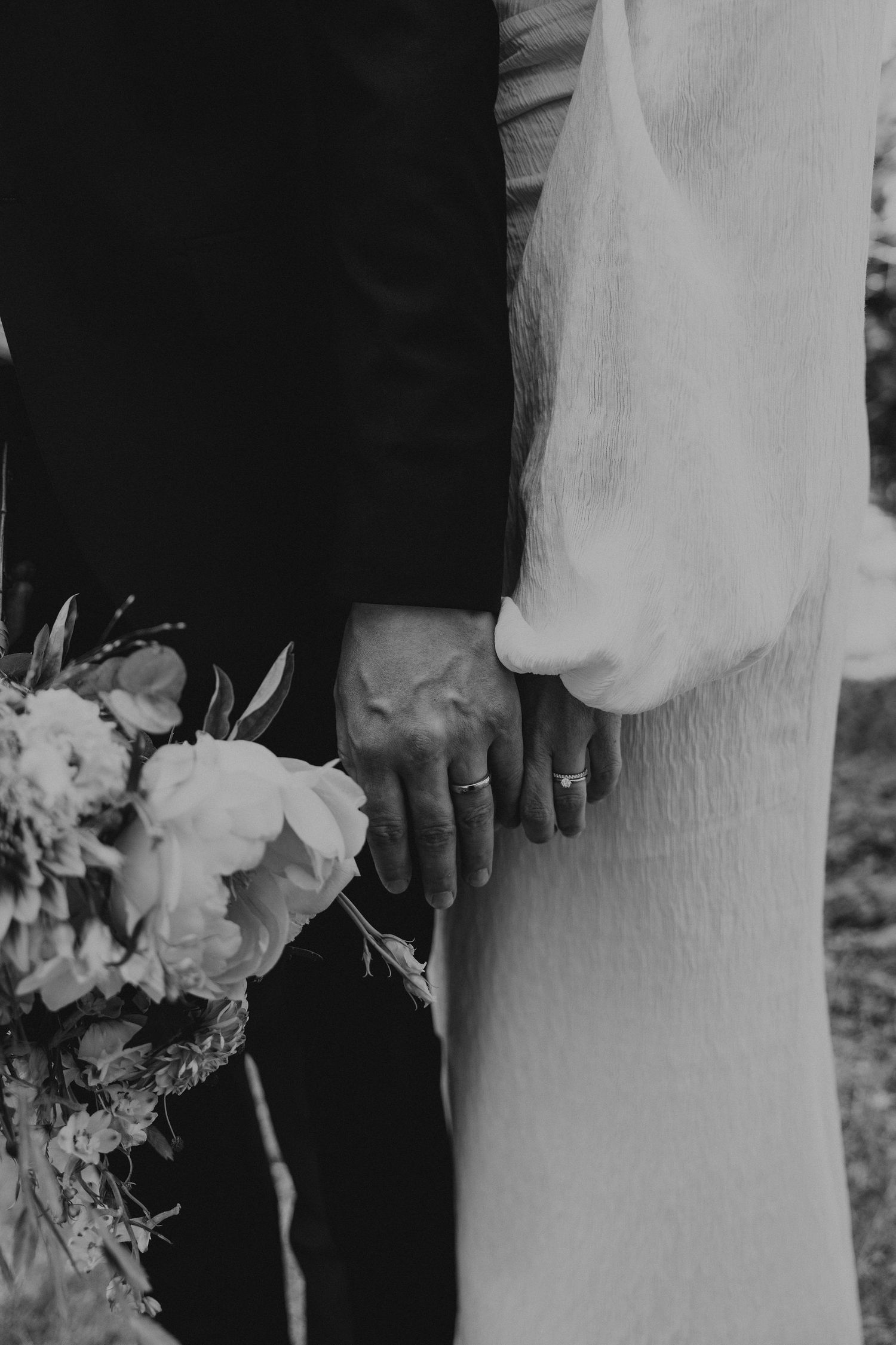 Black and white wedding photo detail showing bride and groom standing side by side with elegant floral bouquet in white.