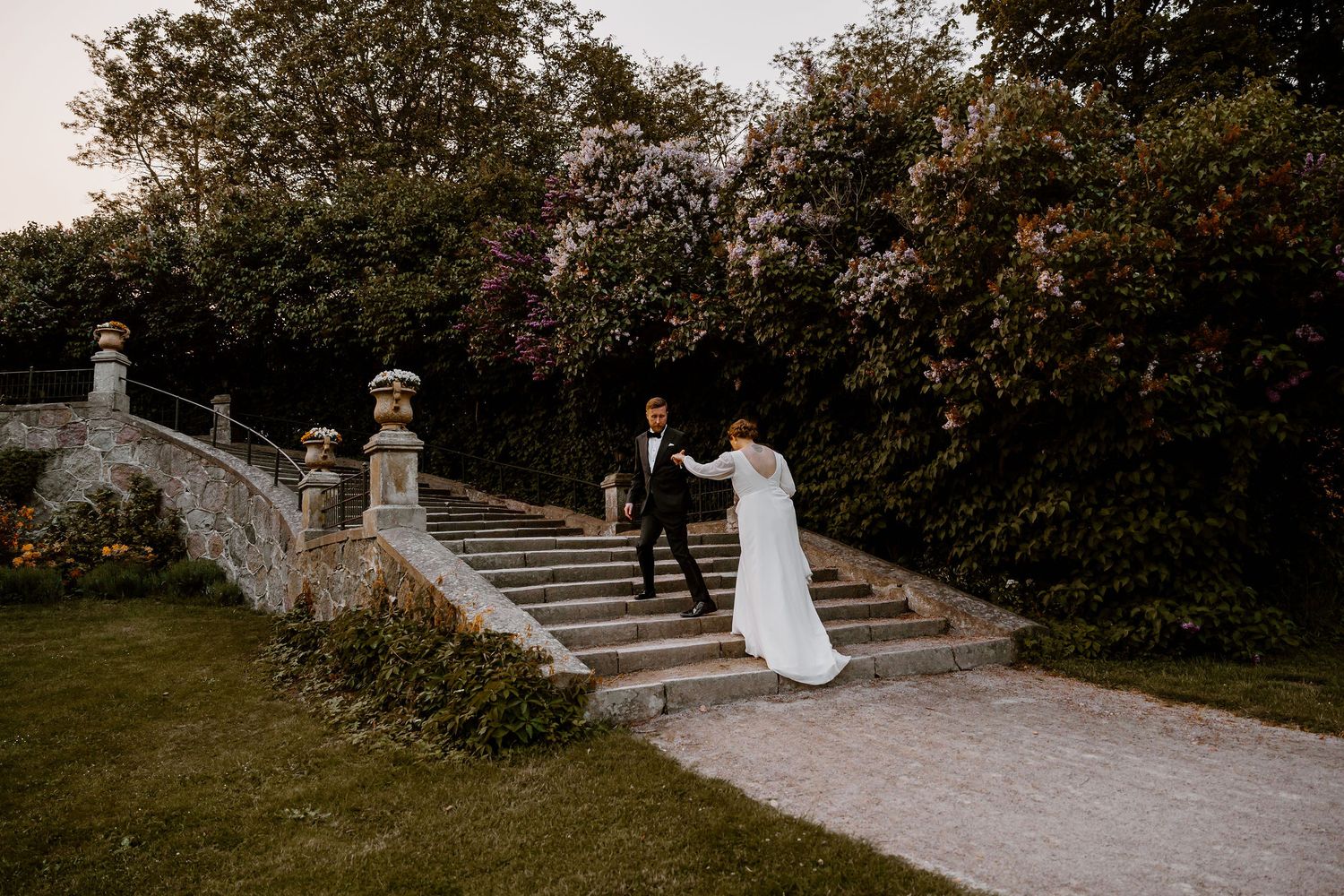 Elegant outdoor wedding photography in a garden setting with a couple walking on stone pathways at sunset.