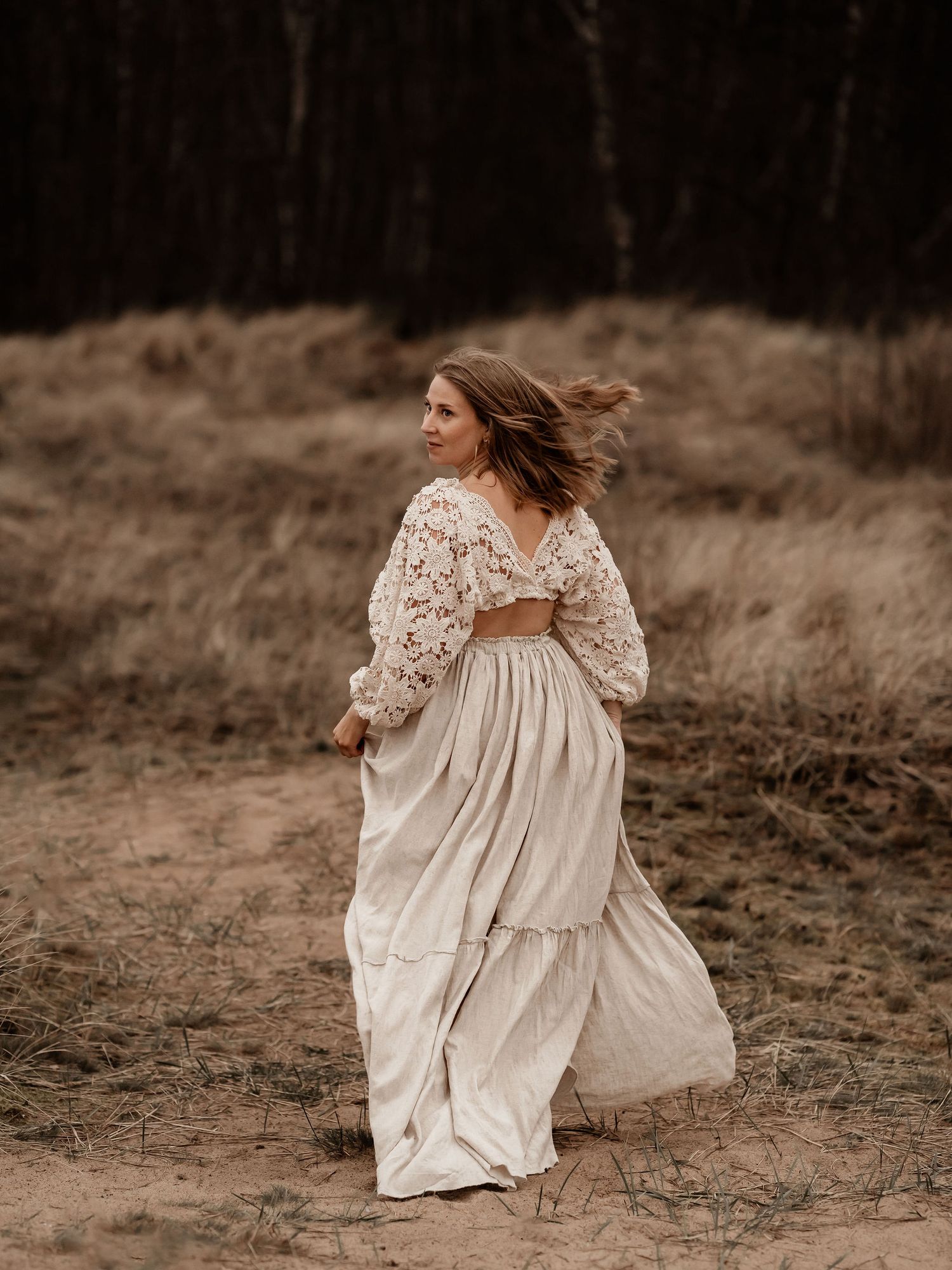 A ethereal figure in a flowing white lace dress twirls gracefully in a moody outdoor setting with windswept hair.
