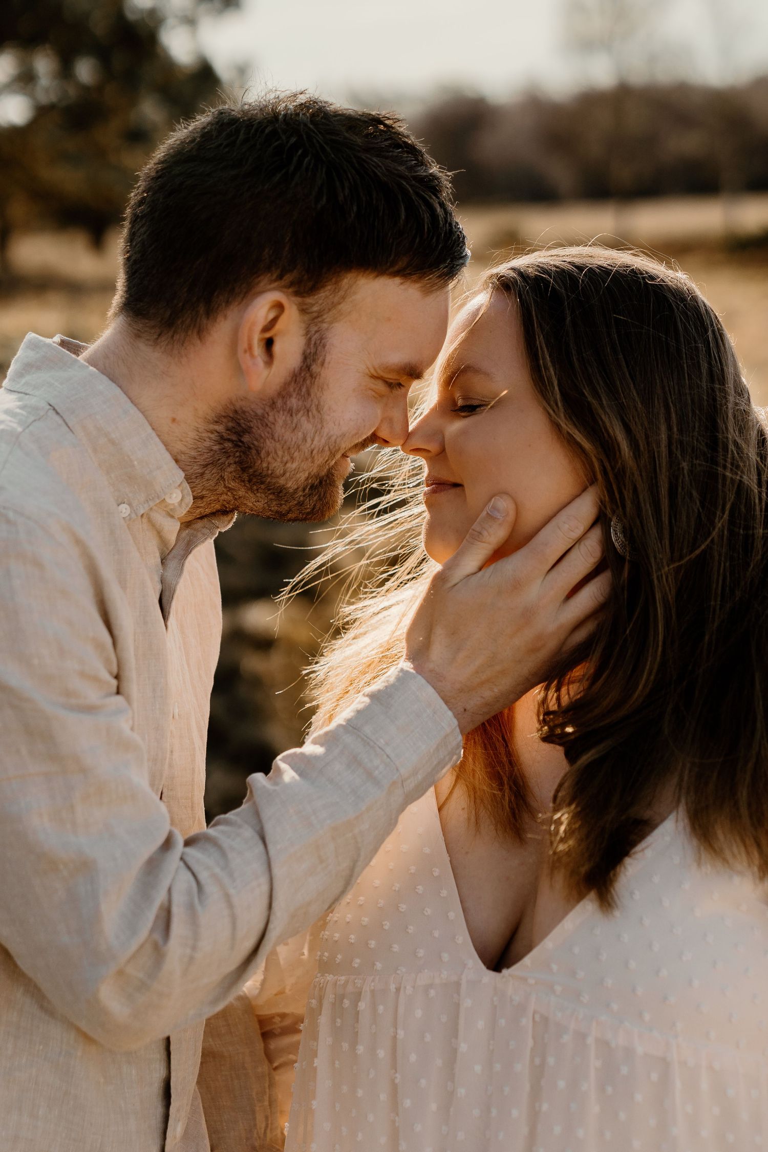 A romantic golden hour photo of a couple in white clothing sharing an intimate moment outdoors.