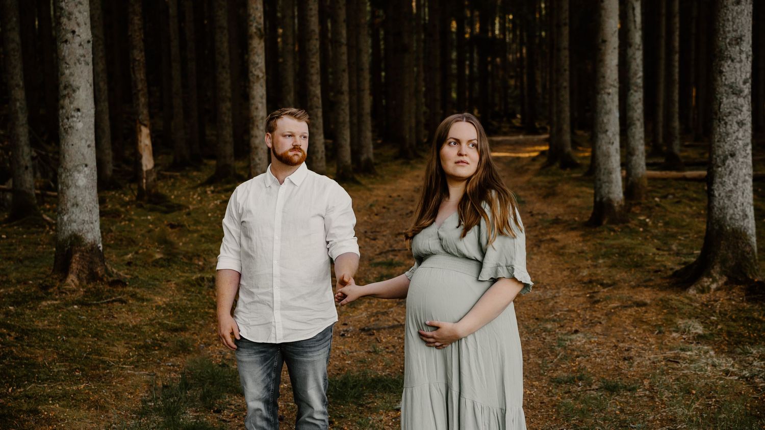 Expectant couple stands together in a serene forest setting during a maternity photo session.