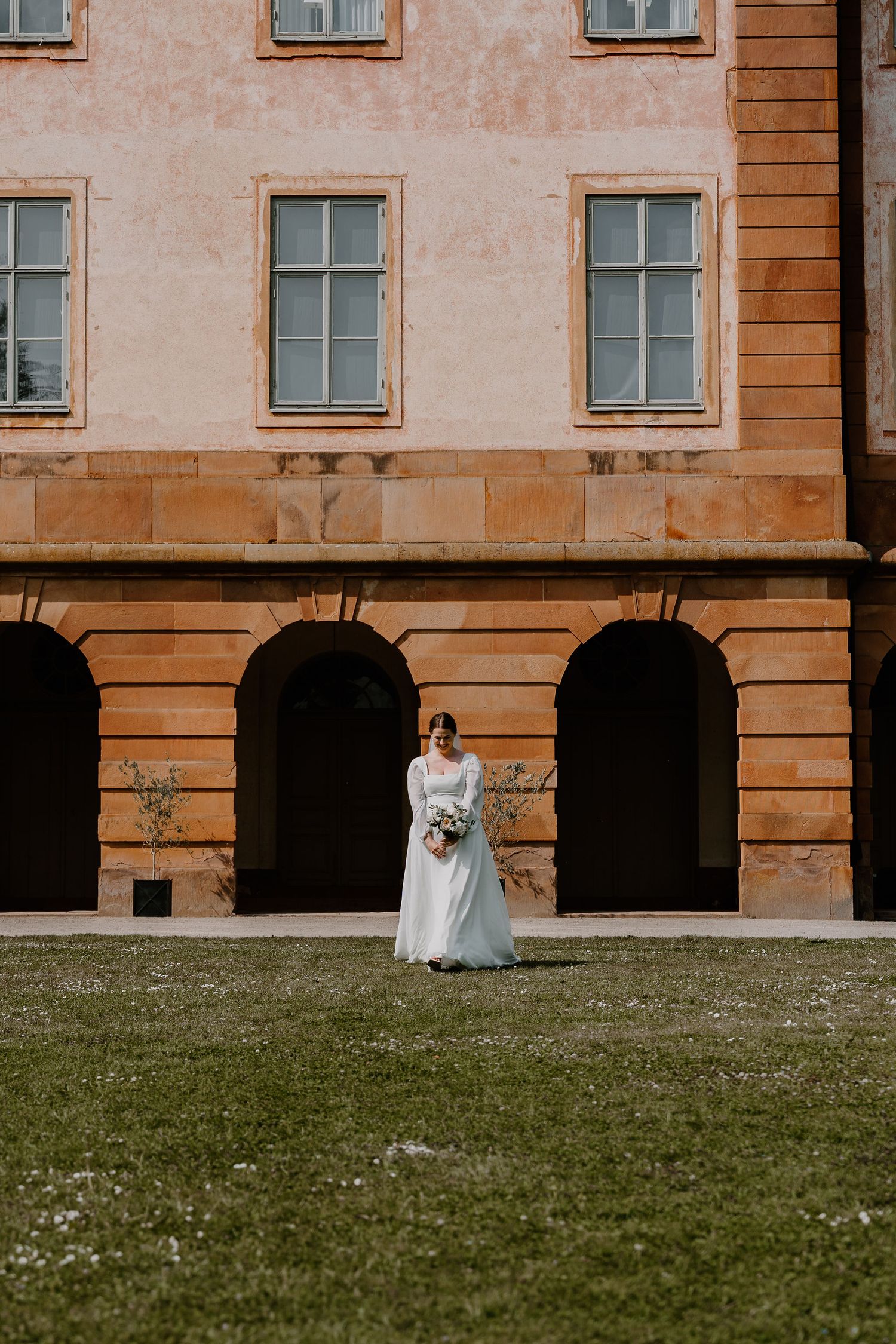 A panoramic view of a vintage building facade with stone columns and grassy lawn in warm golden light.