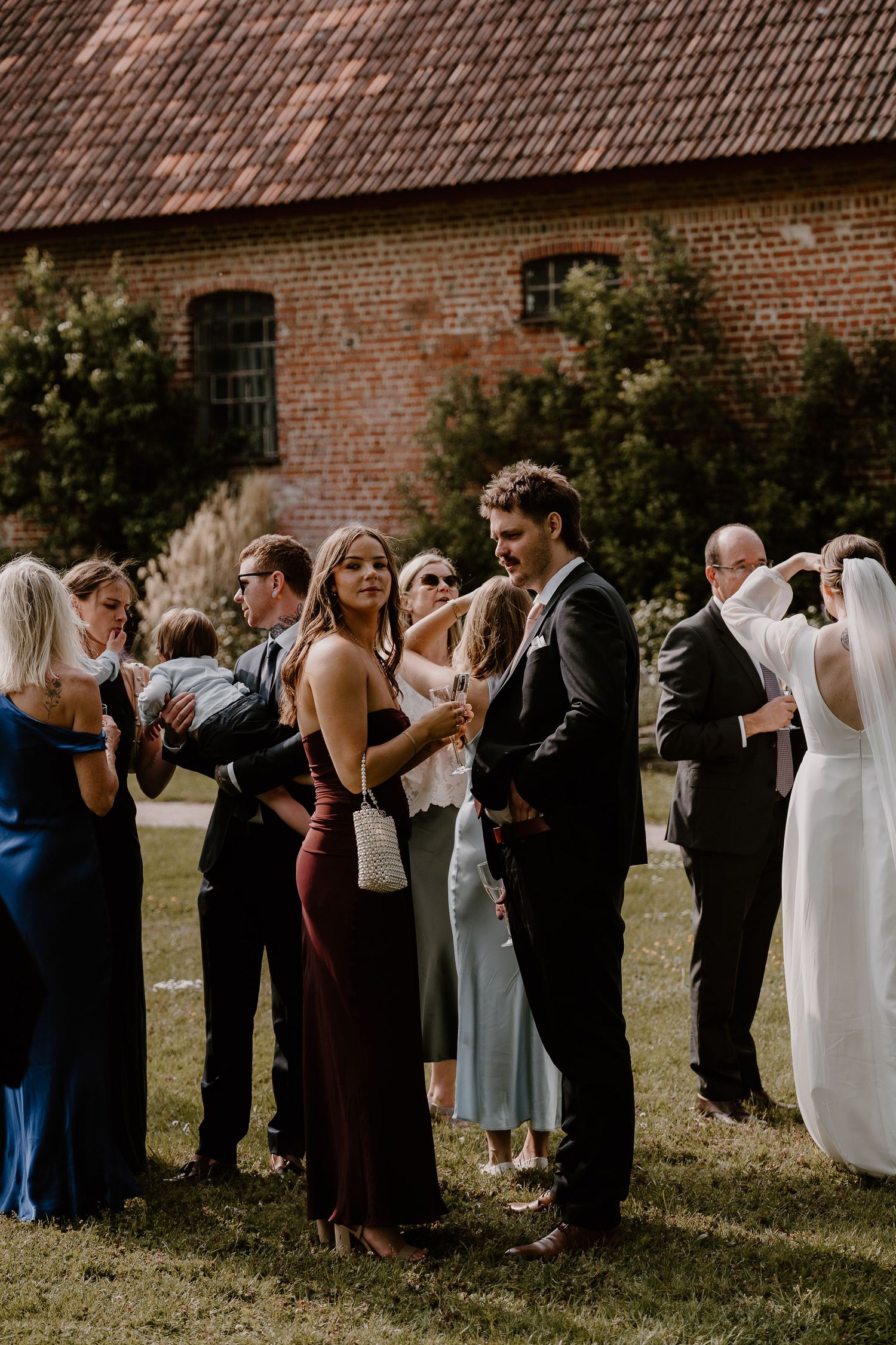 Wedding guests stand in a line outdoors against a brick wall to greet the newlyweds during a receiving line at the ceremony.