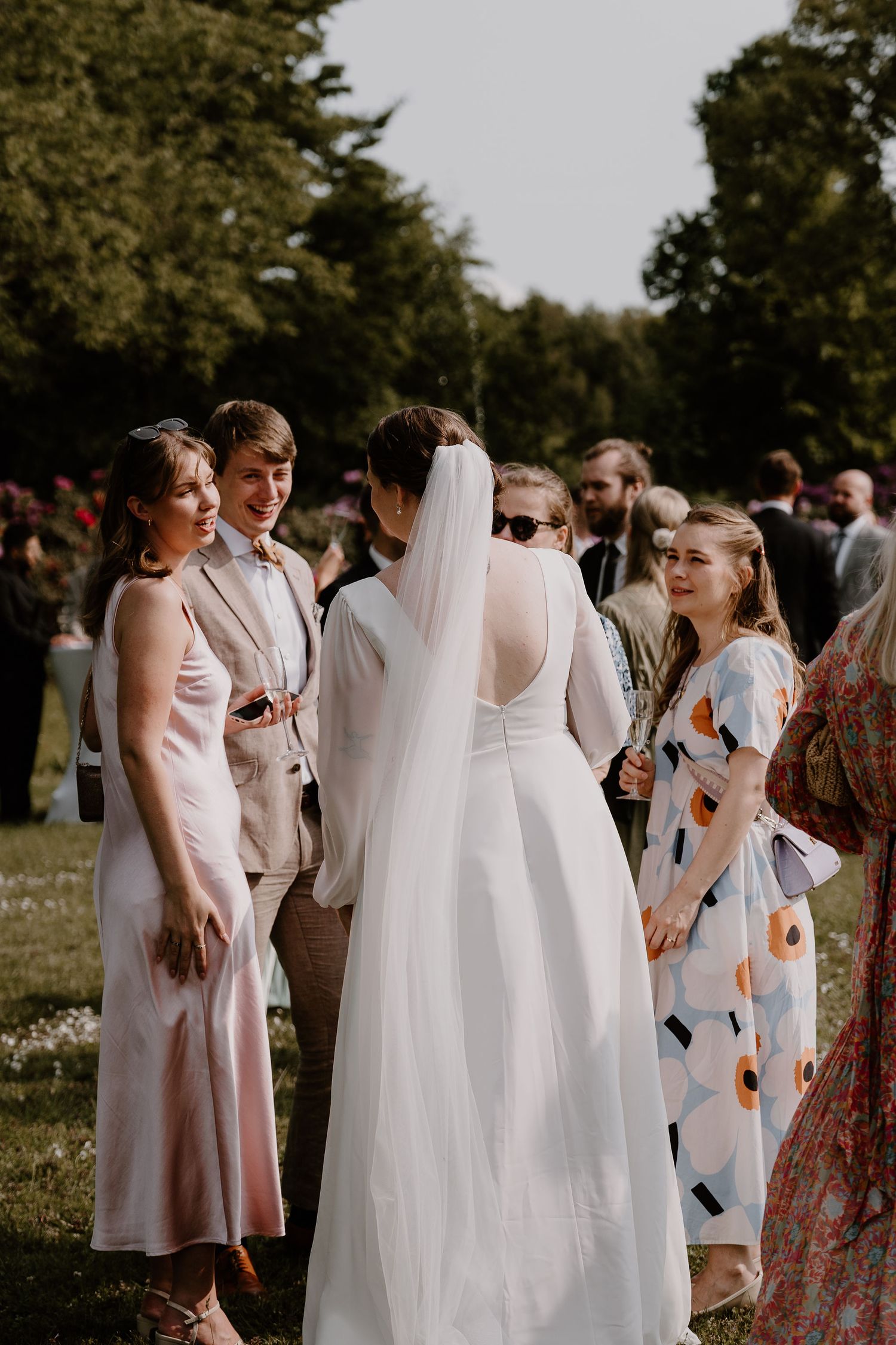 Wedding party members in pink and white dresses gather outdoors at a summer celebration.