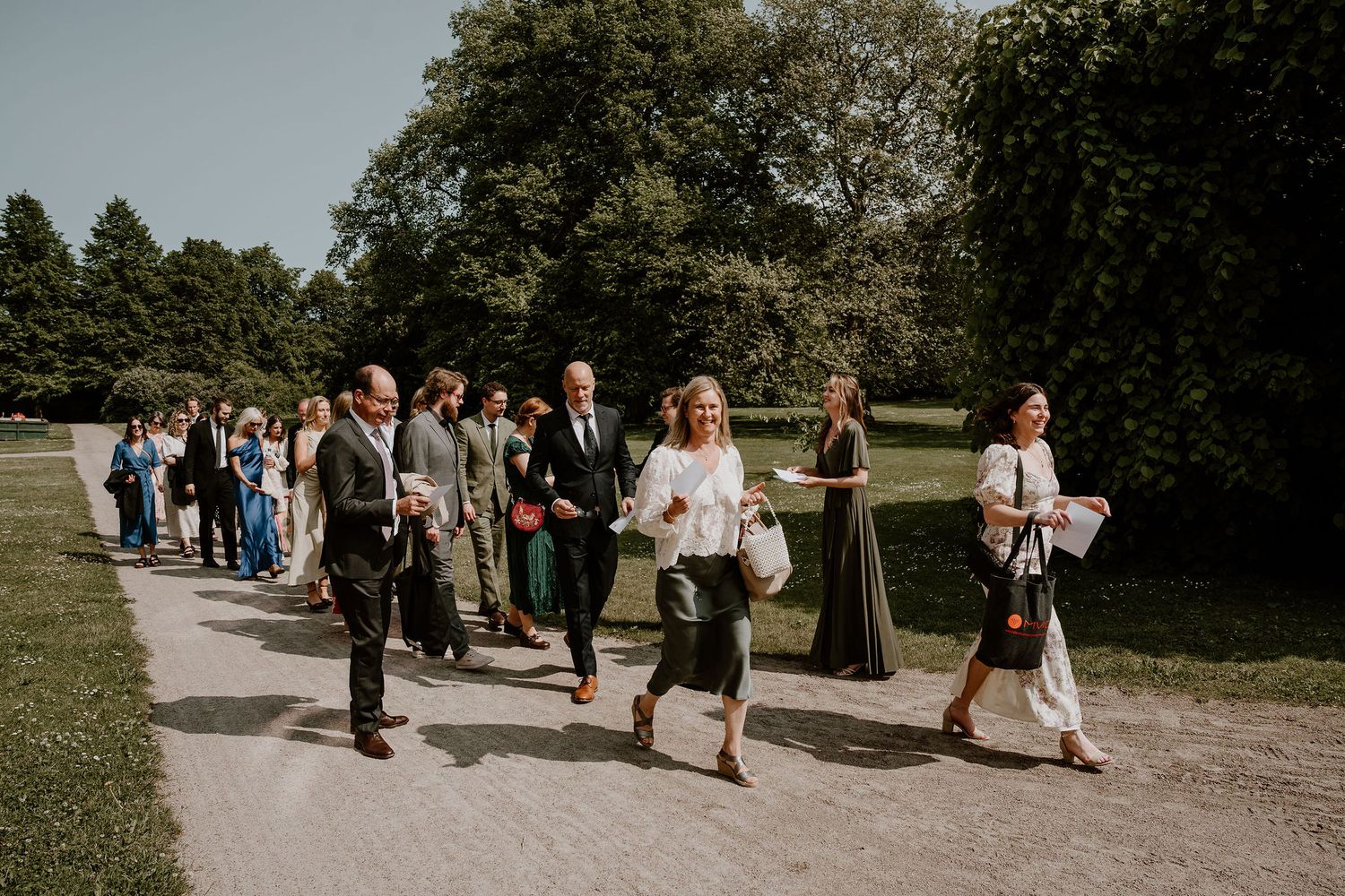 People walking on a scenic garden path surrounded by lush greenery and trees during an outdoor event.