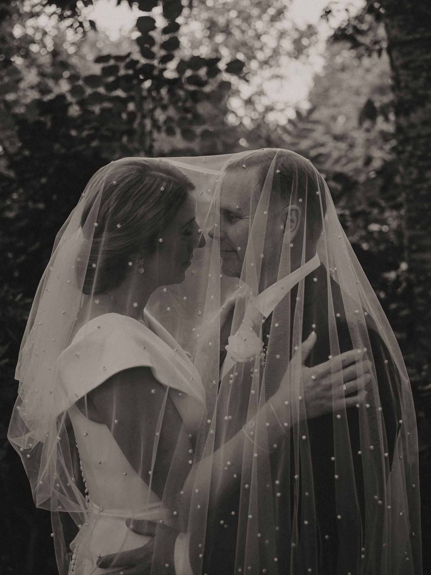 A romantic black and white photograph of a couple sharing an intimate moment under a delicate veil with sparkles.