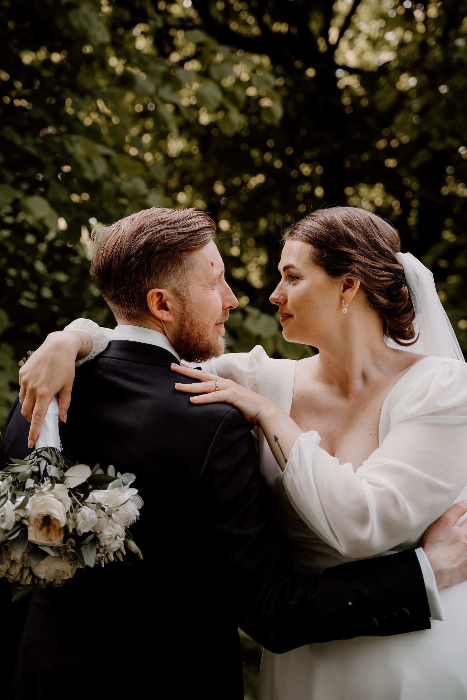 A newlywed couple shares an intimate moment in a garden setting with white floral bouquet and bridal veil.