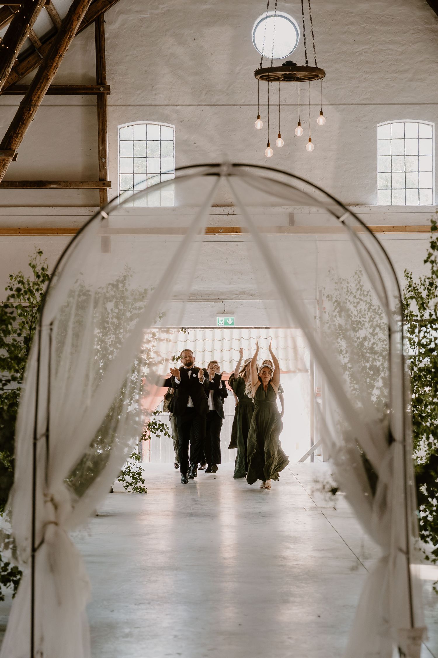 Wedding party celebration captured through an elegant white archway decorated with delicate florals in a bright venue.
