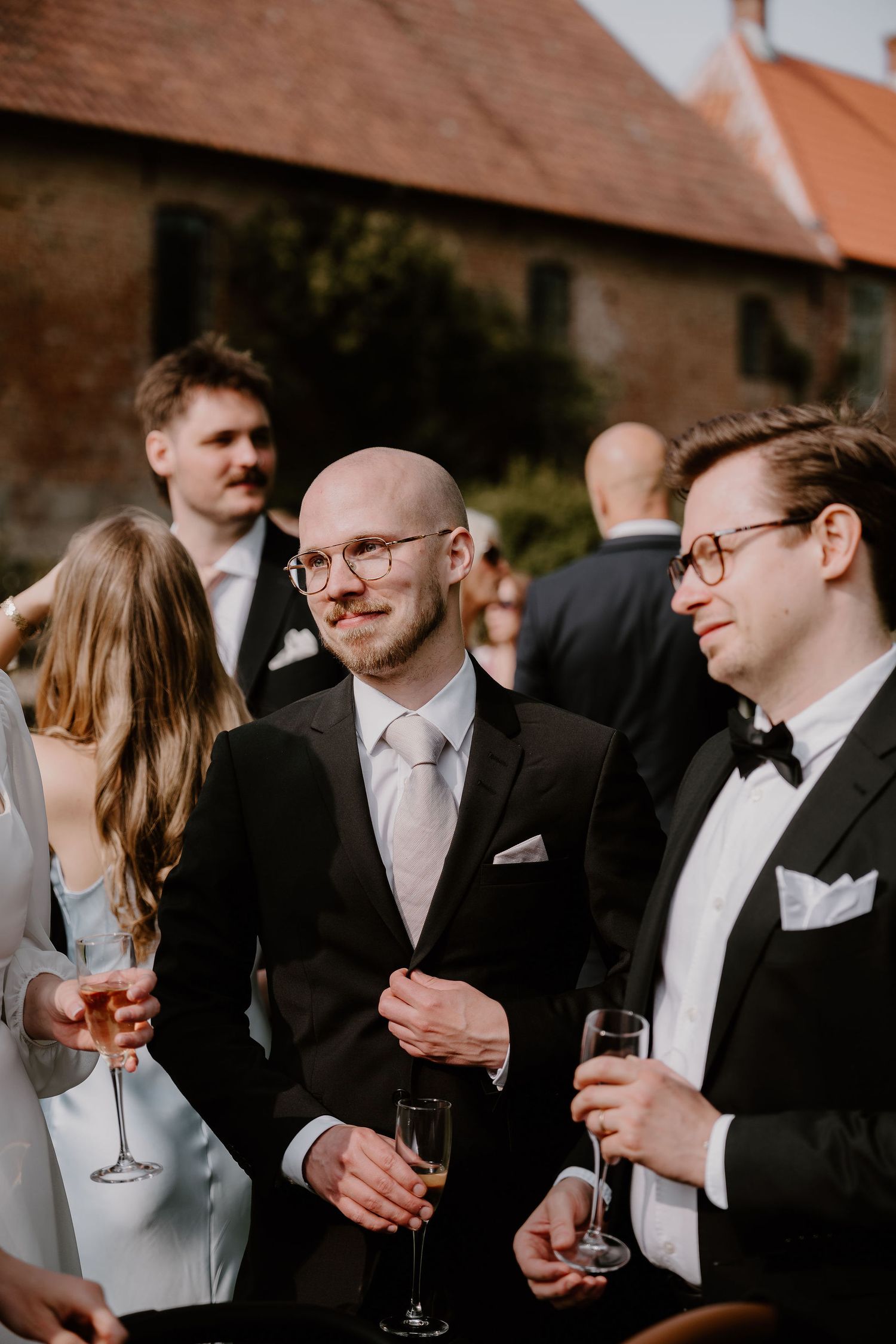 Wedding guests in formal attire enjoying champagne and conversation at an outdoor reception.