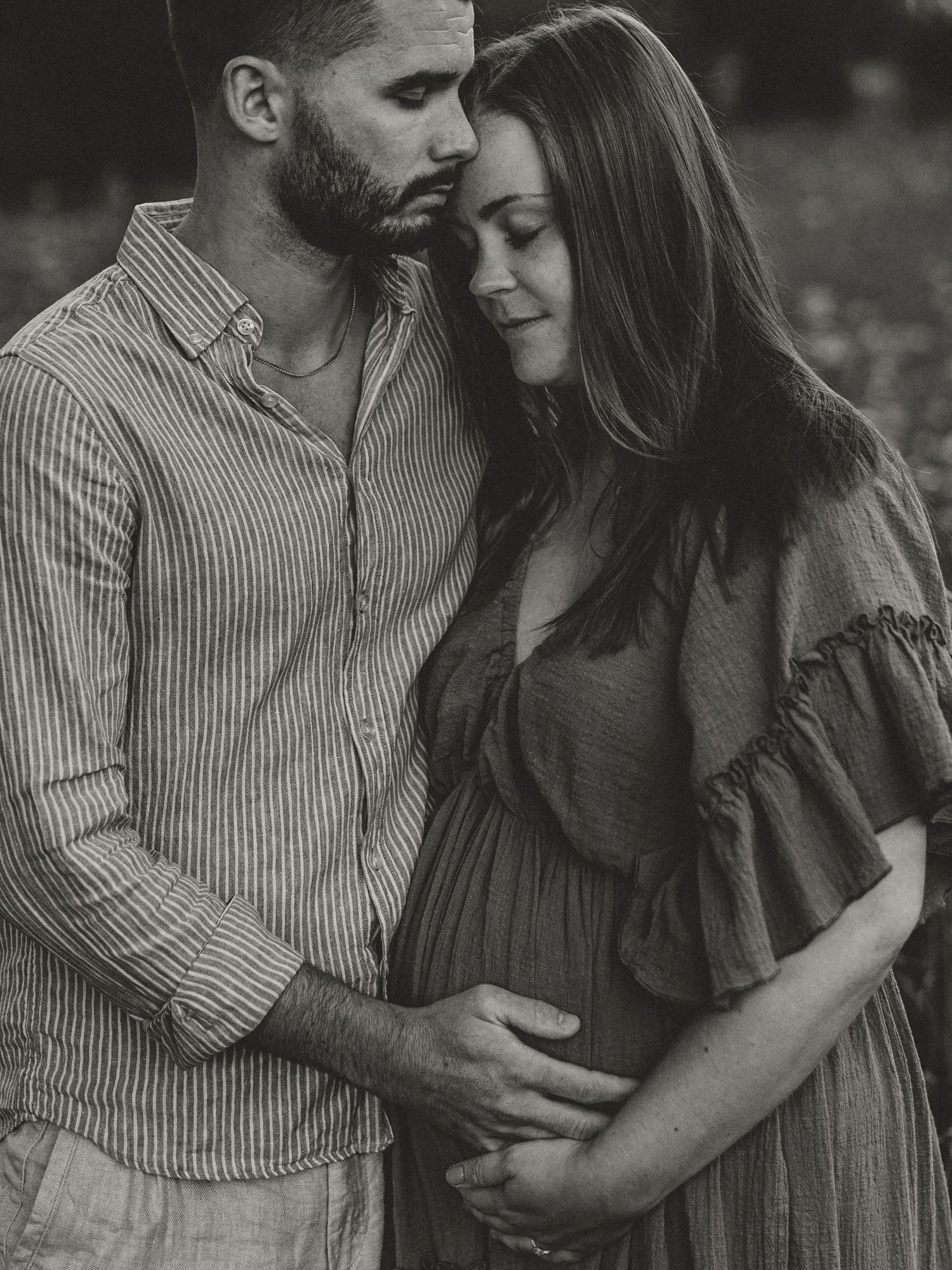 An intimate black and white maternity photo showing a couple embracing outdoors.