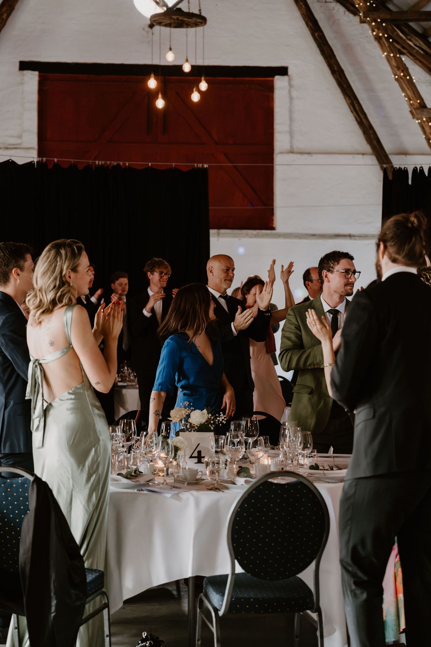 Wedding guests celebrating and dancing around elegant round tables with formal place settings in a rustic barn venue.