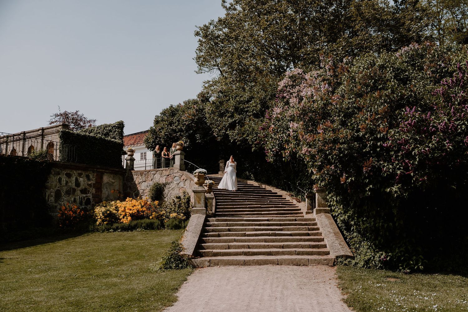 Stone steps lead up a garden path with blooming flowers and trees at a historic estate property.