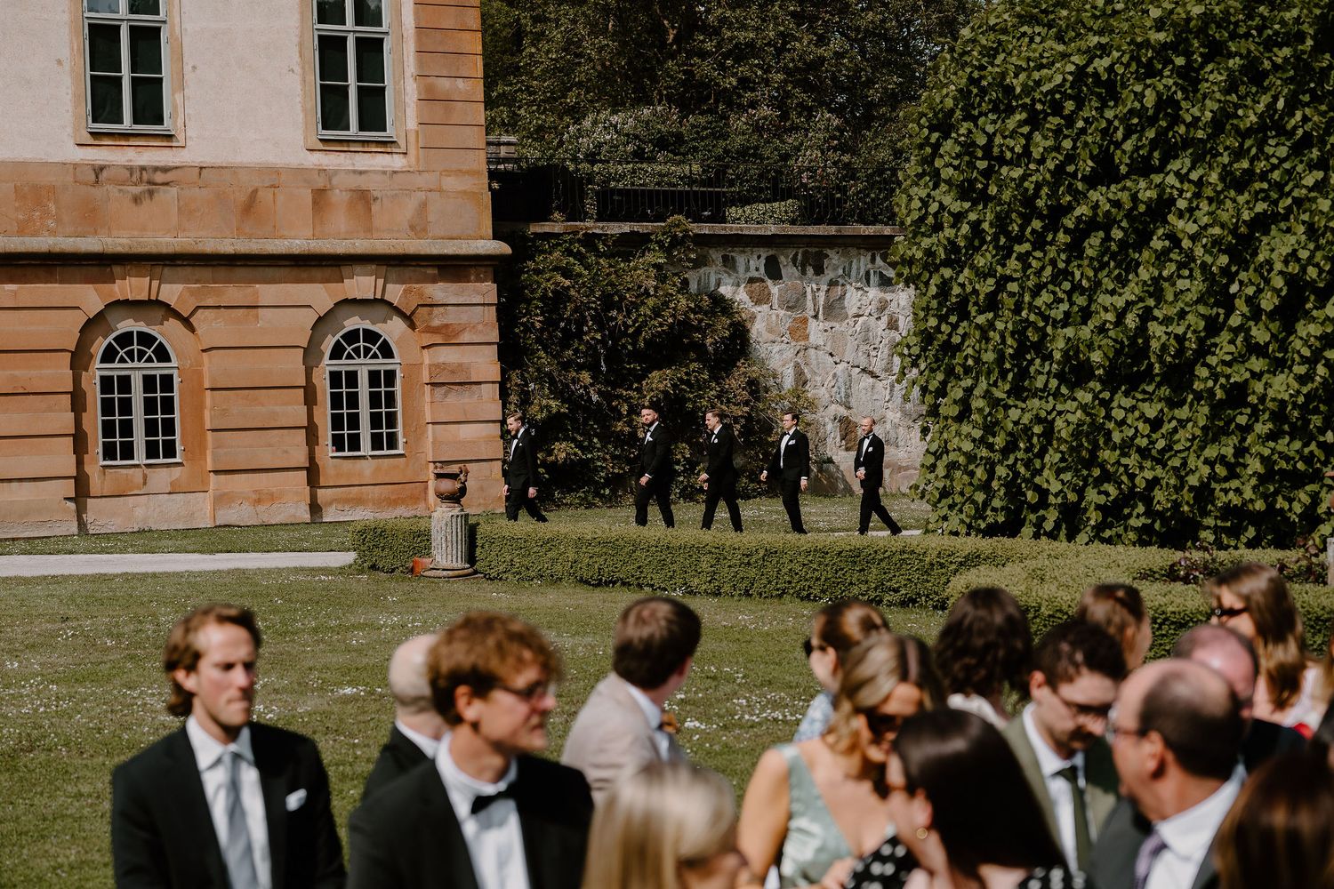 Wedding guests chatting and mingling on a grand estate's lawn during an elegant outdoor reception ceremony.