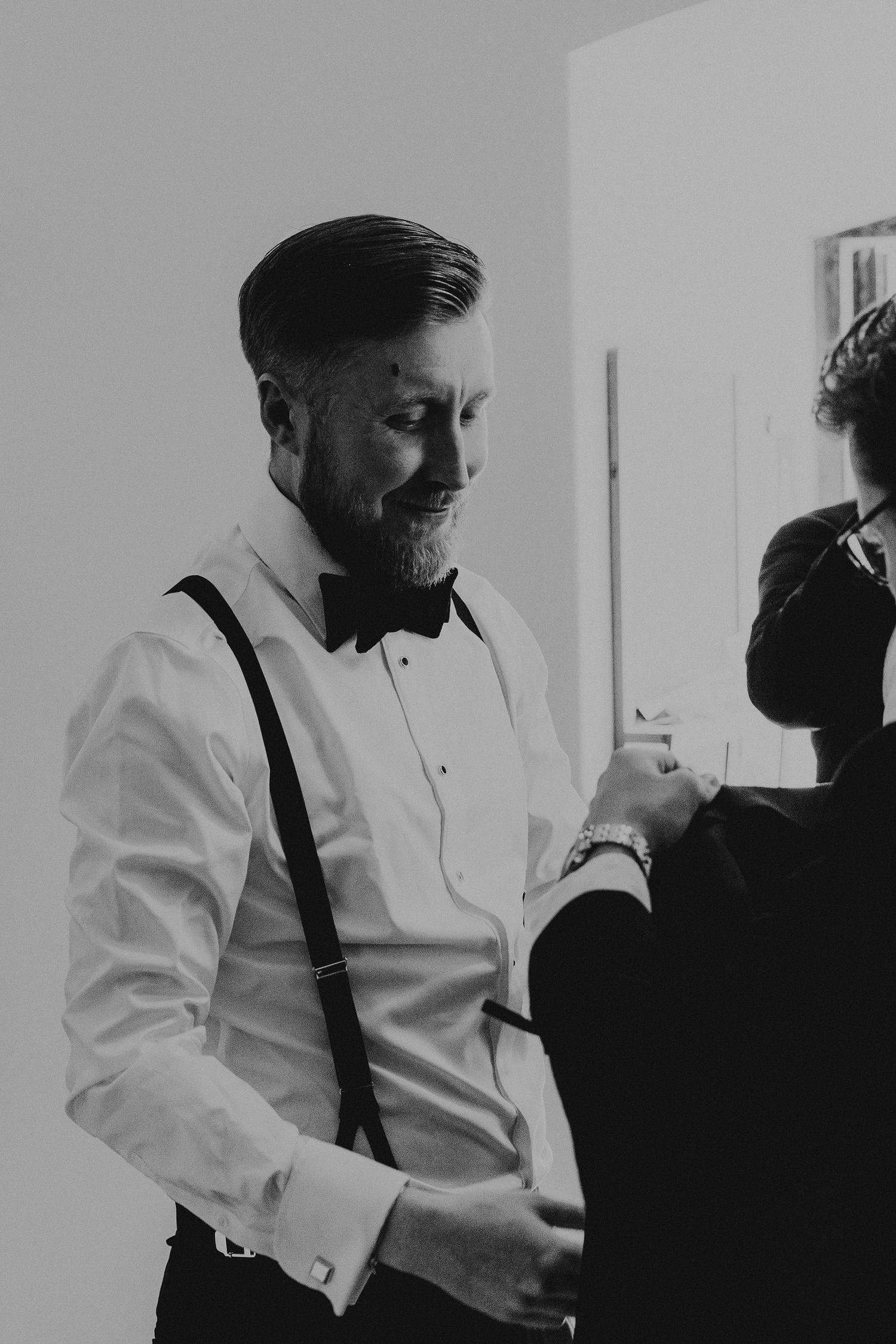 Black and white sequence showing someone in a white dress shirt and dark suspenders preparing for a formal occasion.