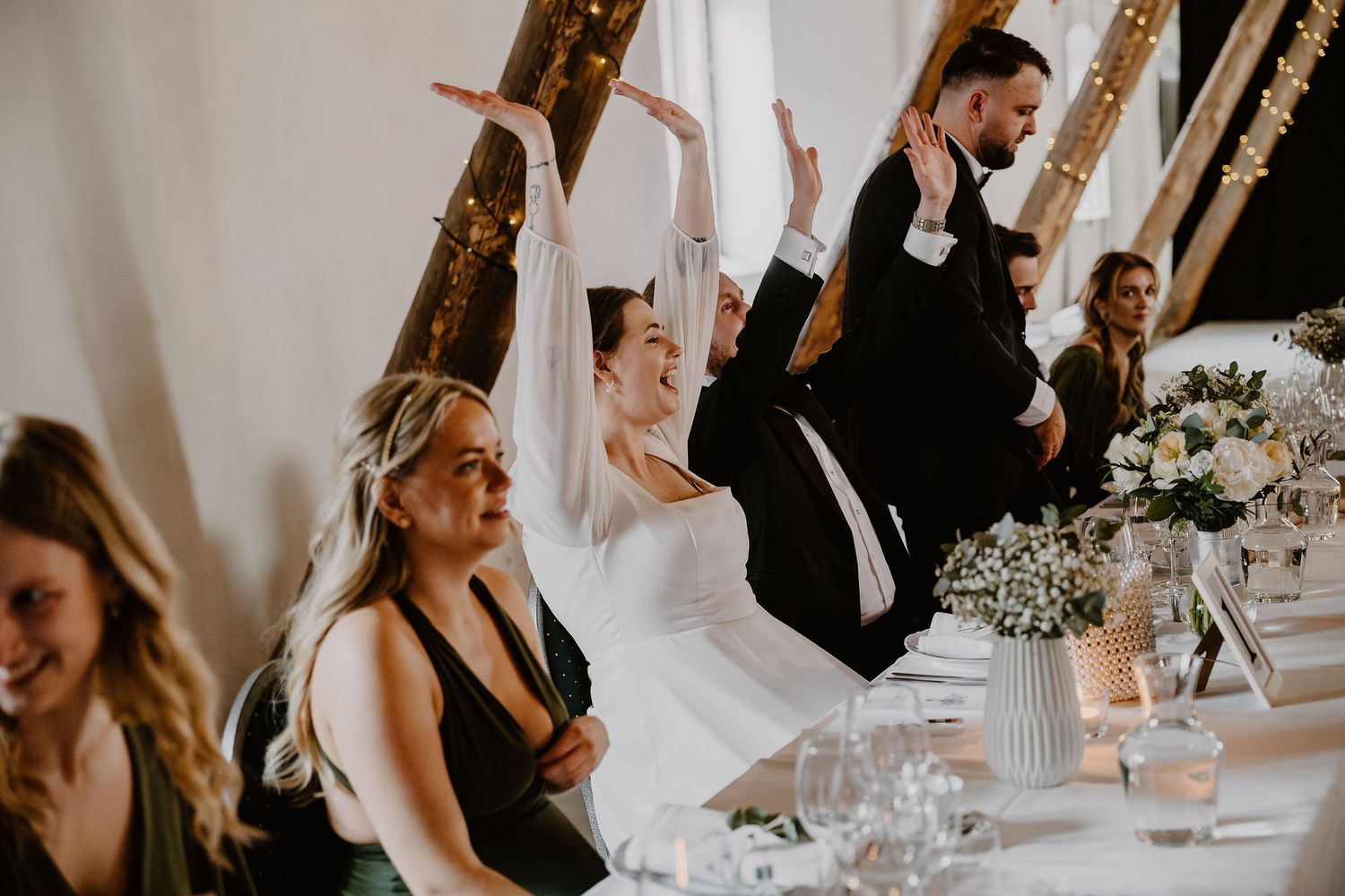 Wedding guests laugh and celebrate during reception dinner at an elegant white tablecloth venue.