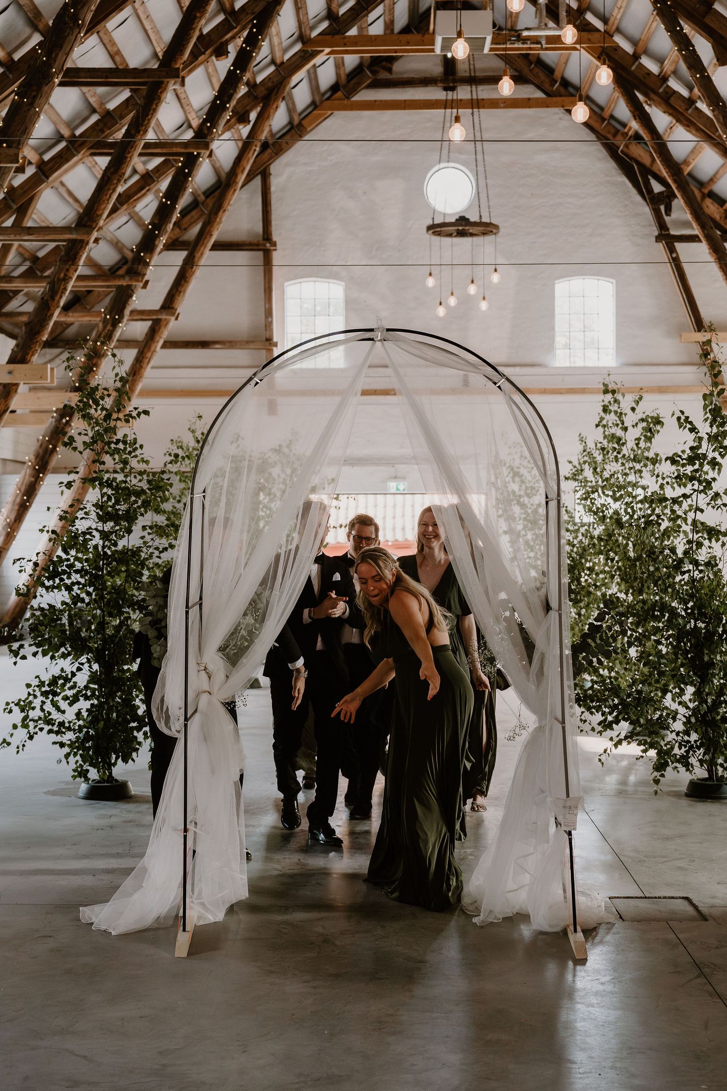 A series of ethereal wedding ceremony photos showing white draped arches in a rustic barn venue with exposed beams and greenery.