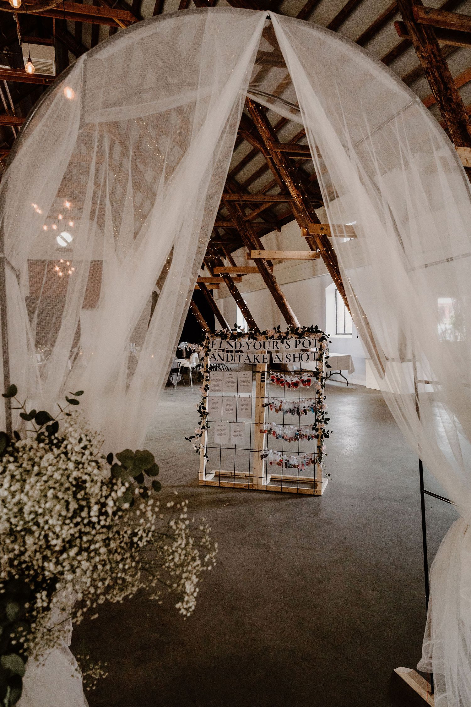 Rustic wedding venue interior with flowing white drapes, exposed wooden beams, baby's breath flowers and hanging displays.