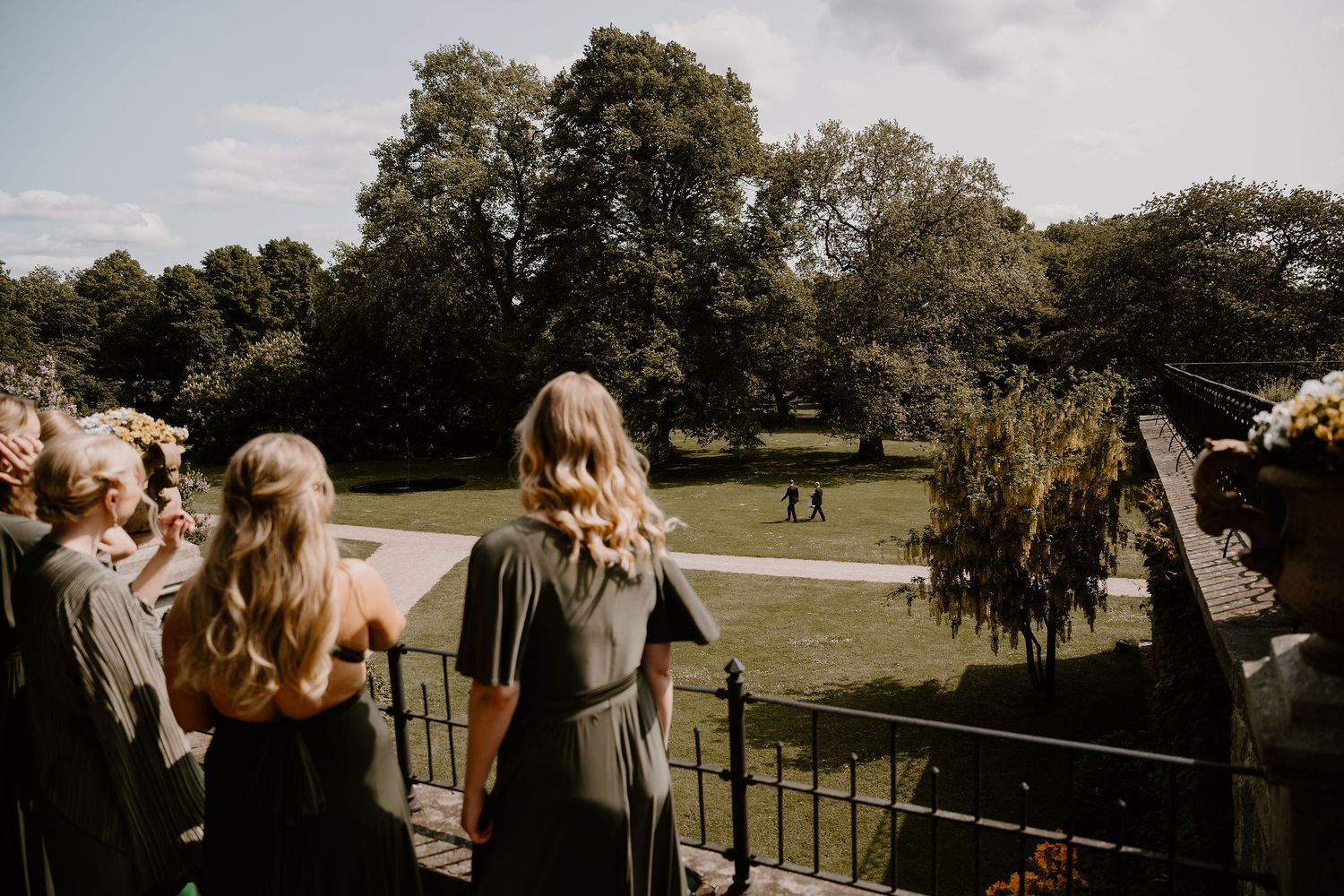 Wedding guests gather on a terrace overlooking a scenic golf course during an outdoor celebration.