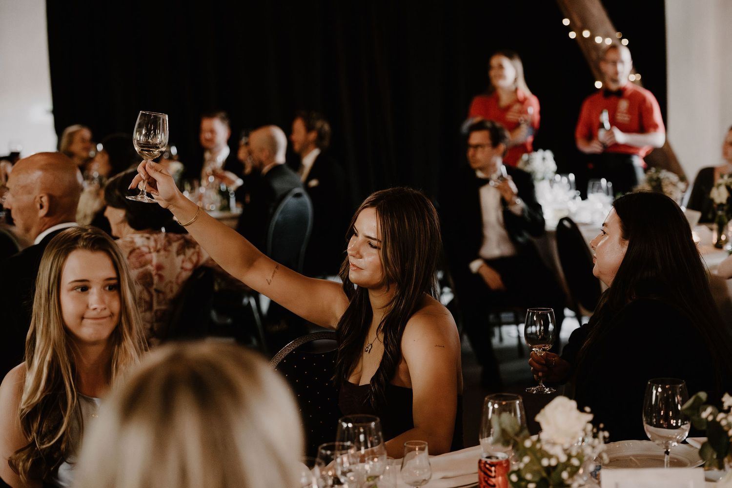 Guests raise their wine glasses in a toast during an elegant indoor wedding reception celebration.