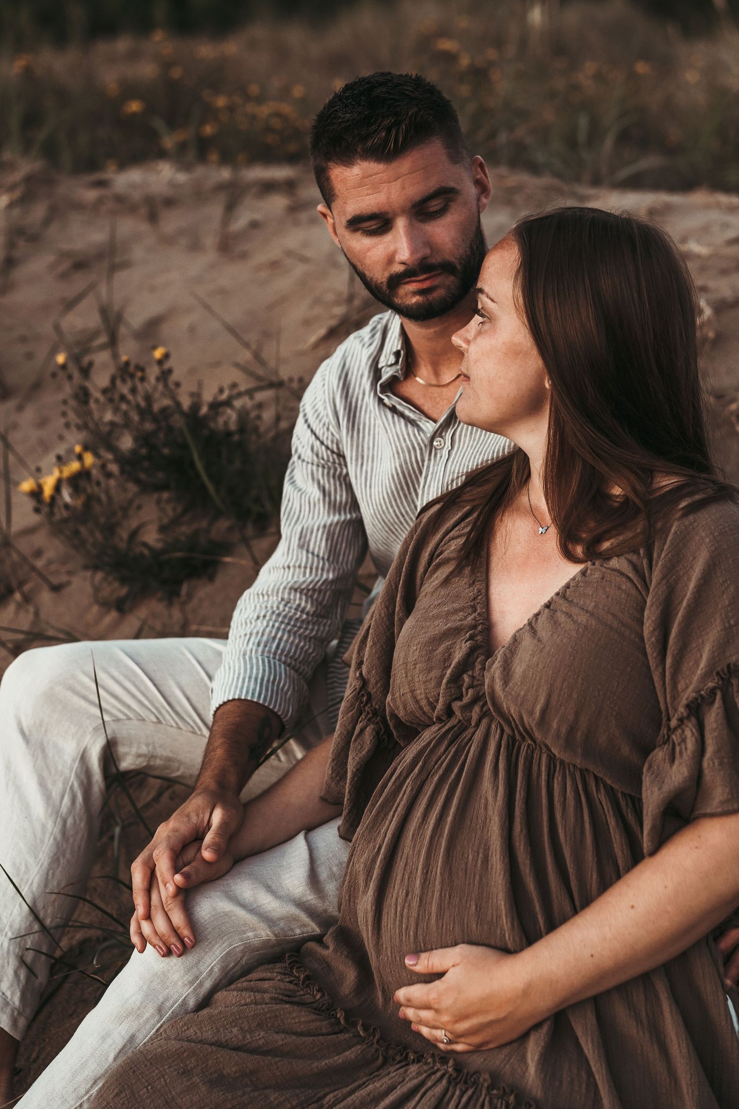 Beautiful maternity photo session outdoors with a couple sitting on a blanket in warm brown tones at sunset.