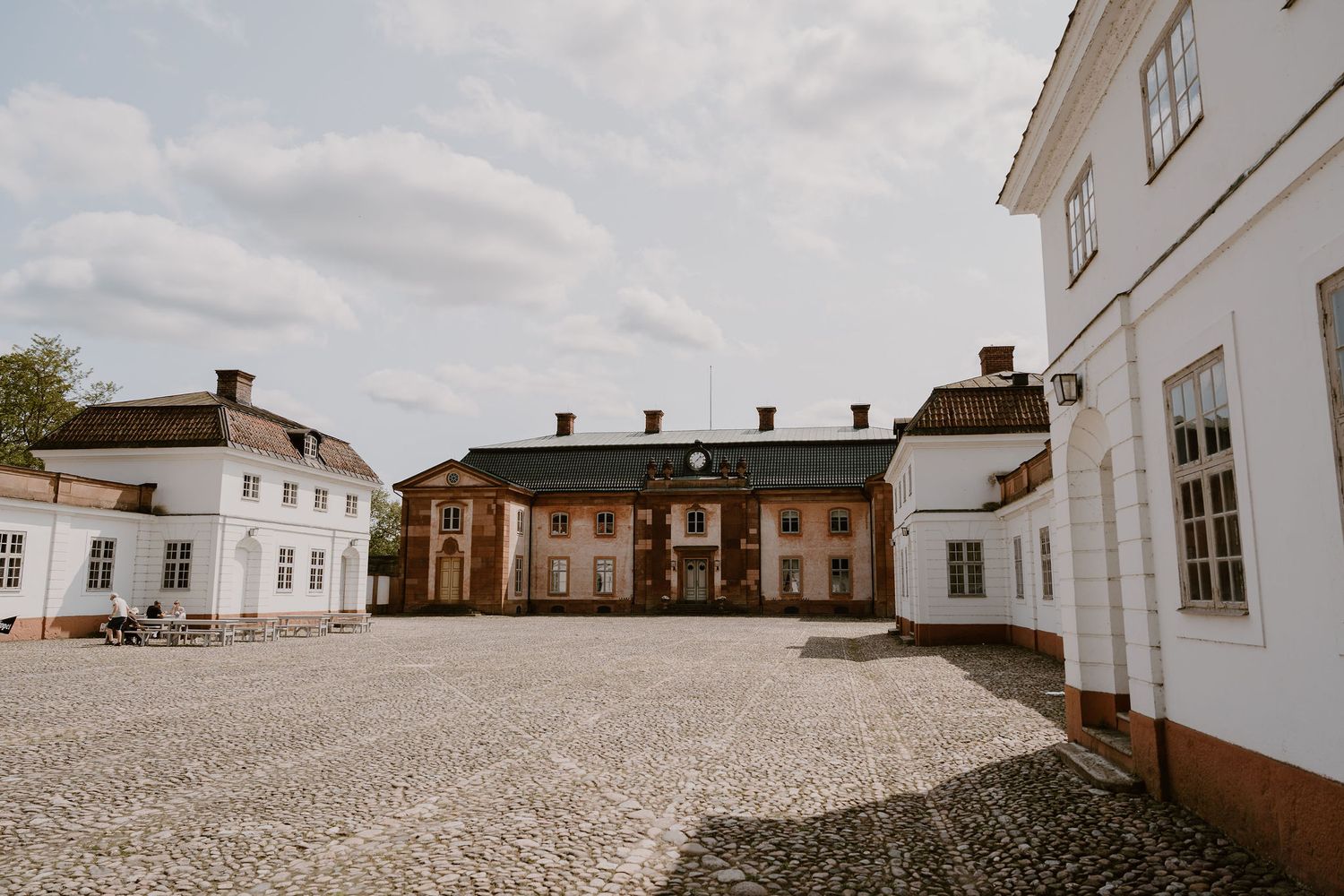Historic white manor buildings with gravel courtyard surround a central brick building in traditional European style.