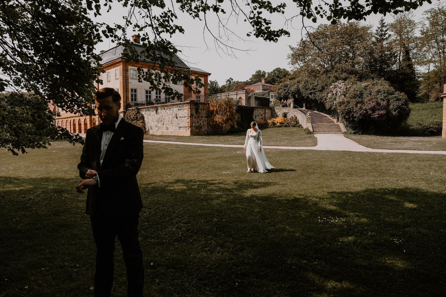 A scenic wedding first look moment captured at a historic estate venue with lush green lawn and grand architecture.