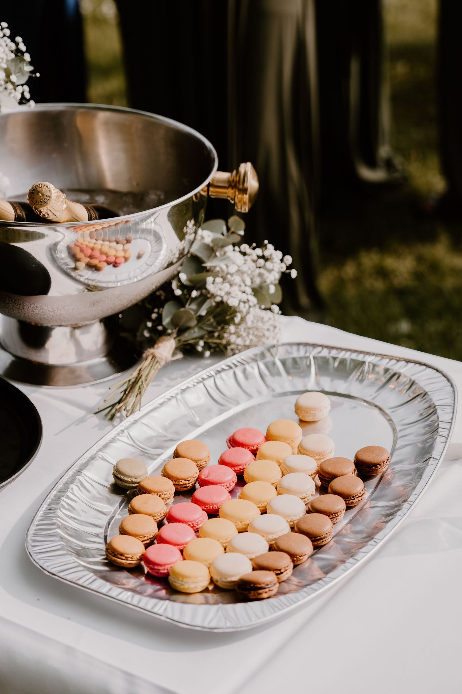 Colorful French macarons arranged on a silver platter with an ice bucket and baby's breath flowers in the background.