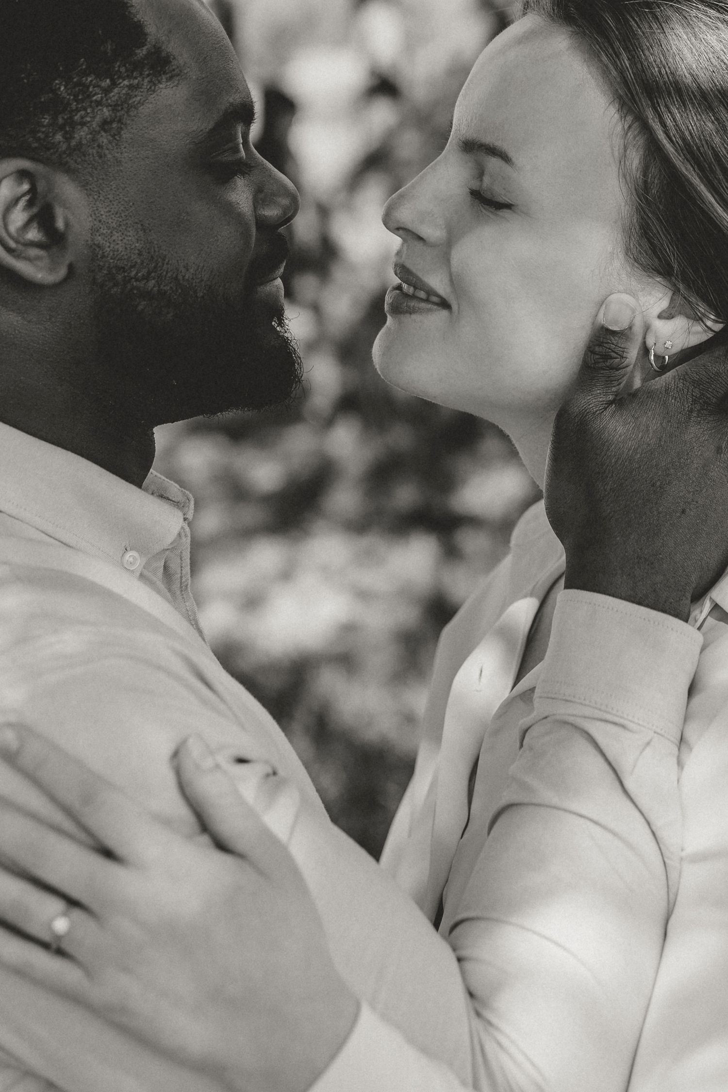Intimate black and white photo of couple in white shirts embracing and sharing a tender romantic moment outdoors.
