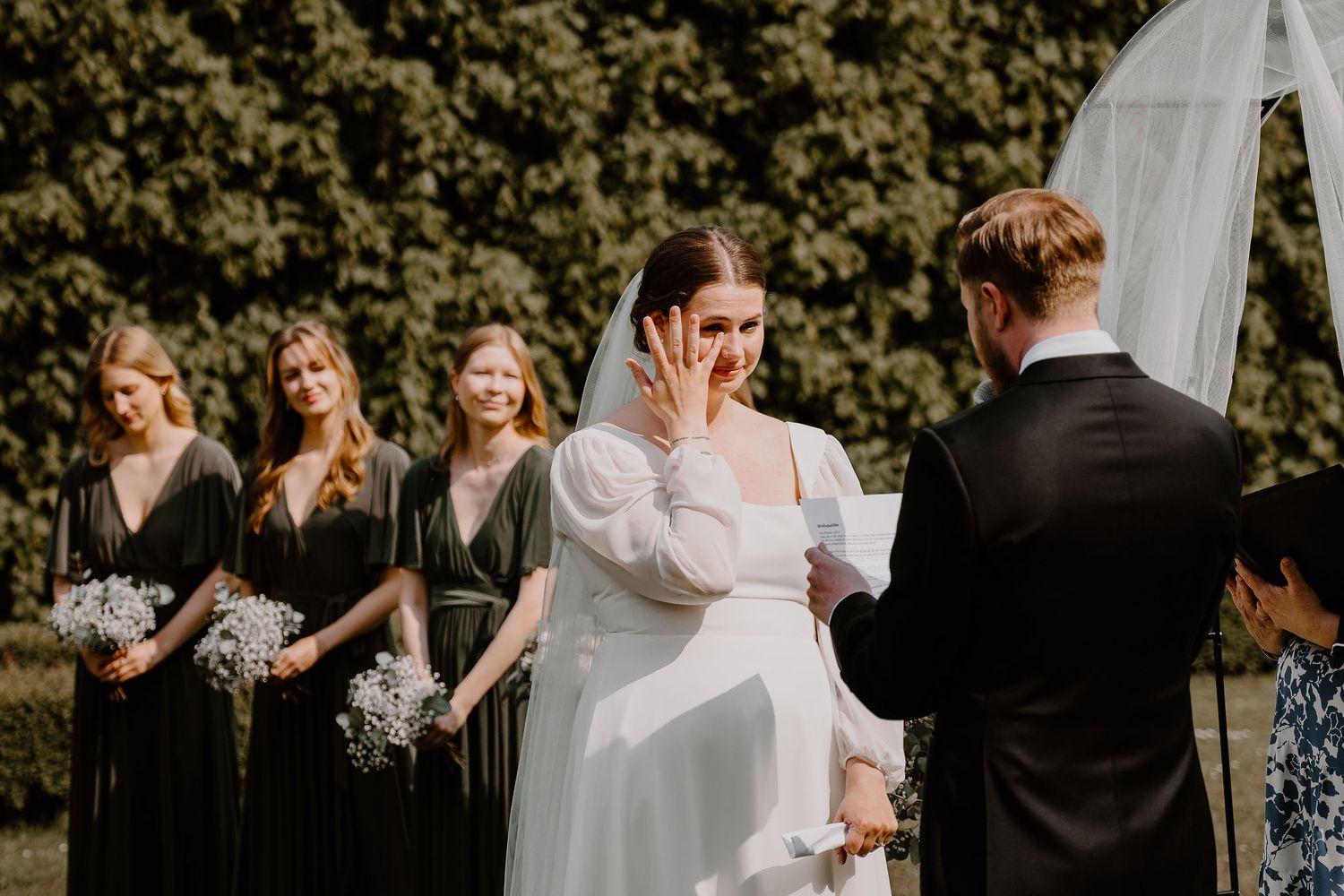 Wedding party celebrates during golden hour, dancing in a lush garden setting in formal attire.