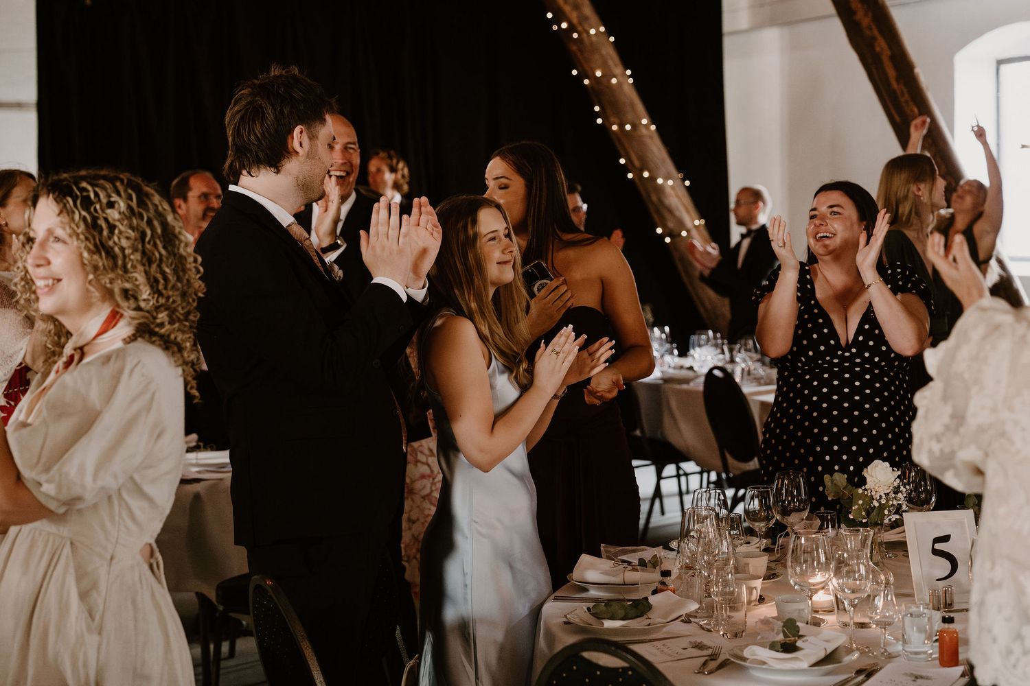 Wedding reception guests clap and cheer excitedly during a celebratory moment at an evening event.
