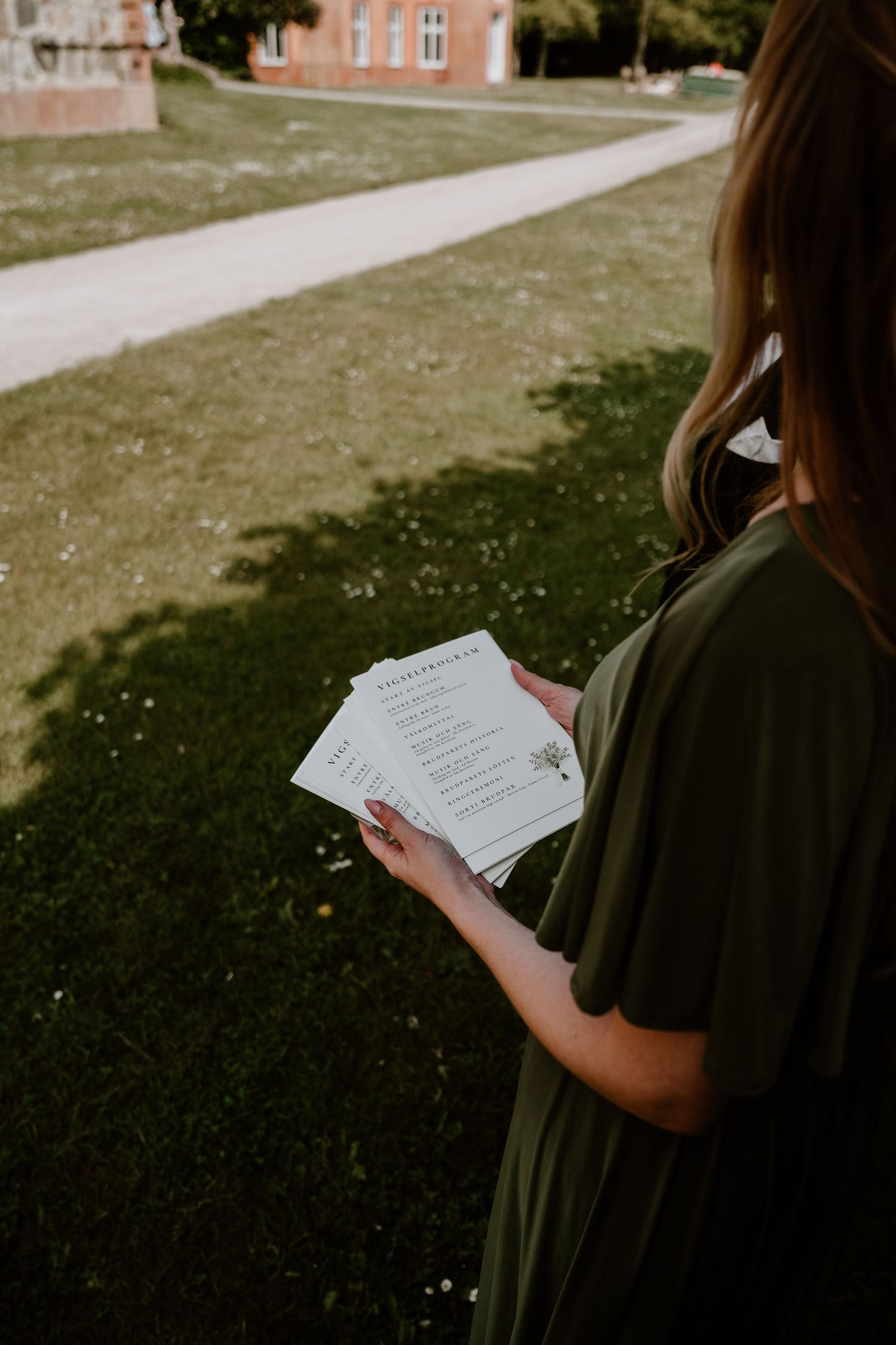 Someone stands on green grass reading notes while wearing an olive green shirt as sunlight streams across the lawn.