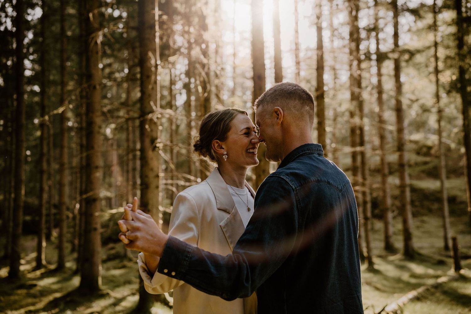 A romantic couple dancing together in a sunlit forest during a golden hour sunset.