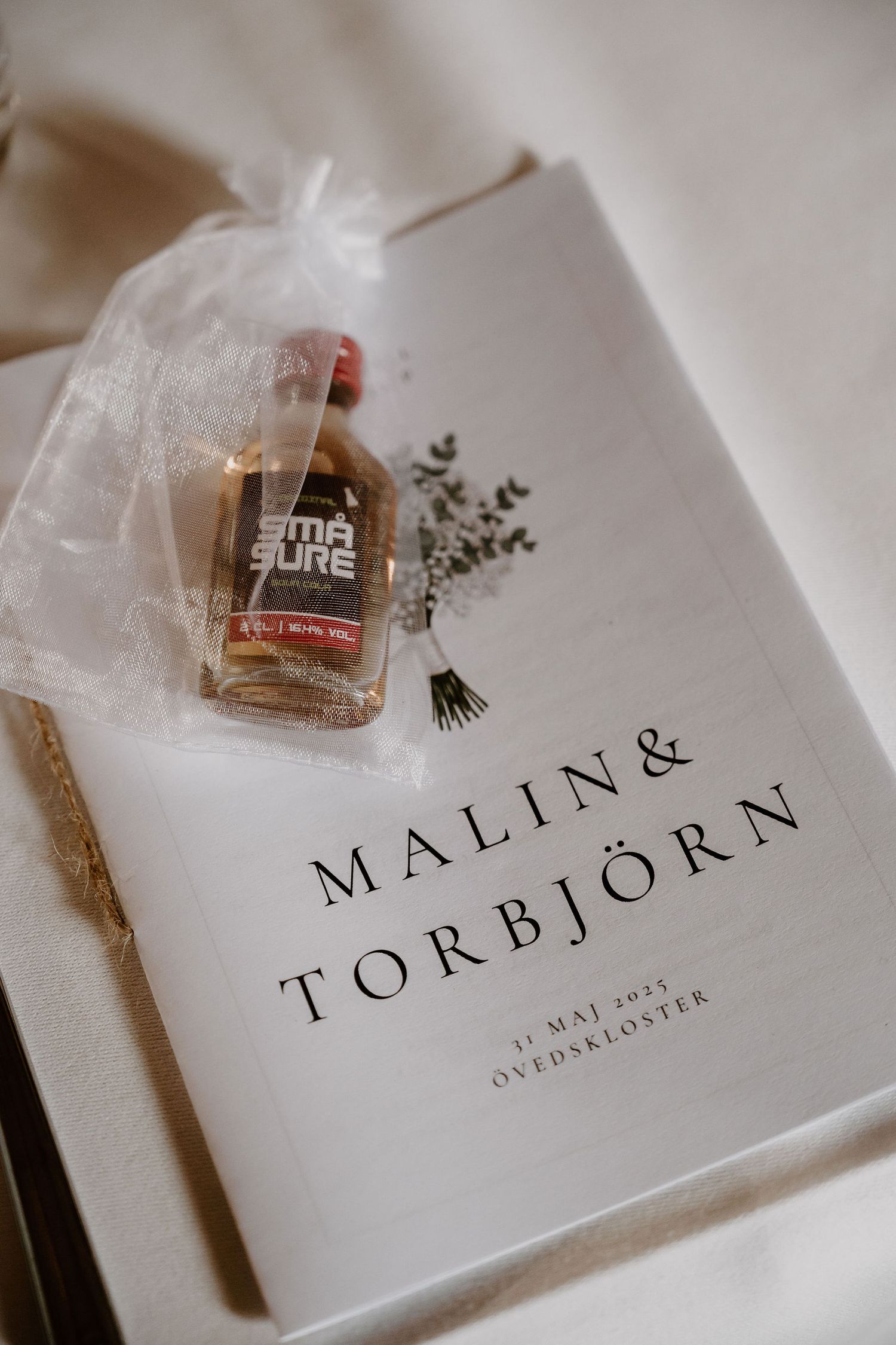 White wedding invitation card with names Malin and Torbjorn displayed next to a small bottle of perfume or fragrance.