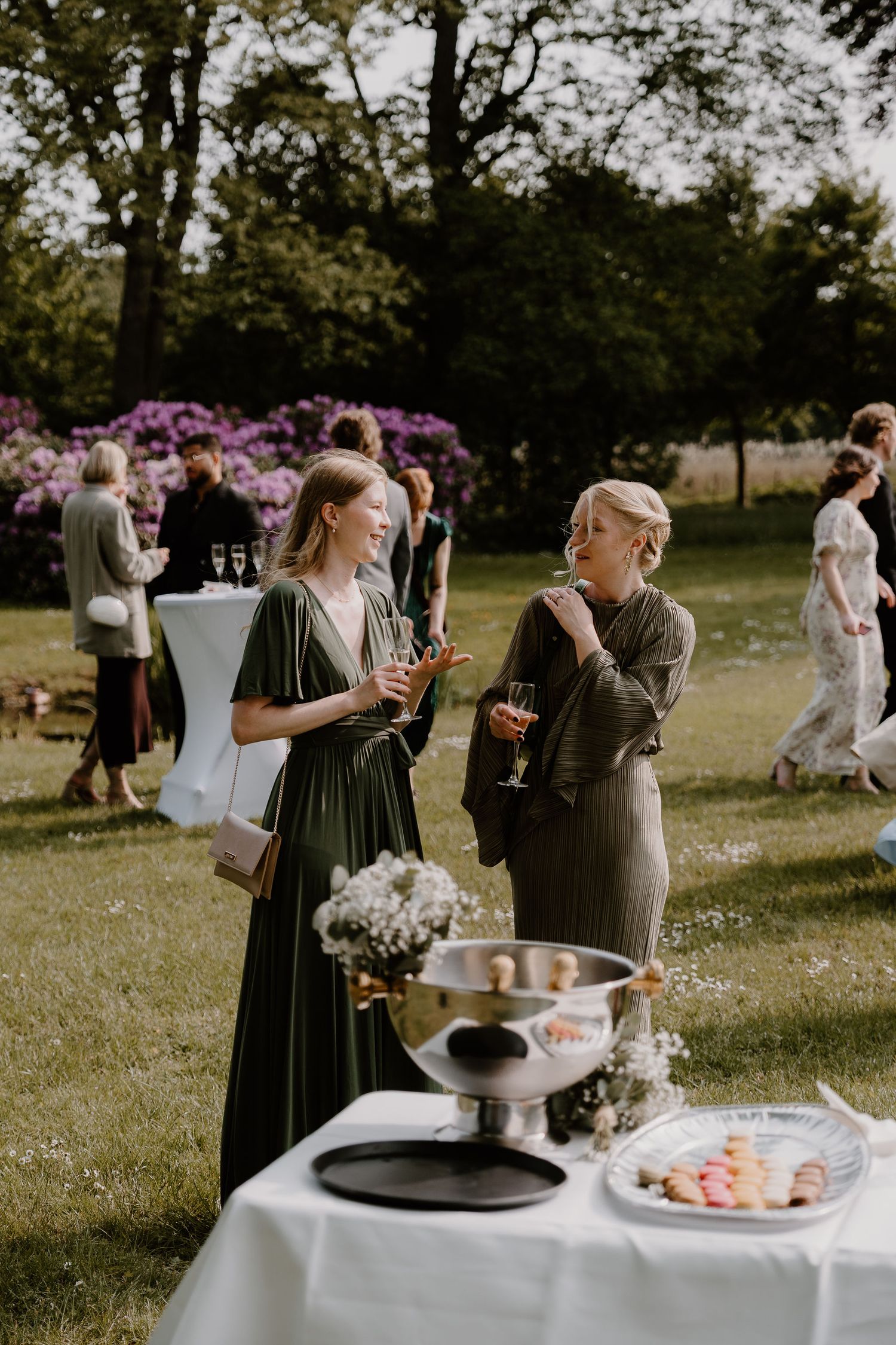 Wedding guests gather at an outdoor reception with tables decorated with floral arrangements and refreshments.