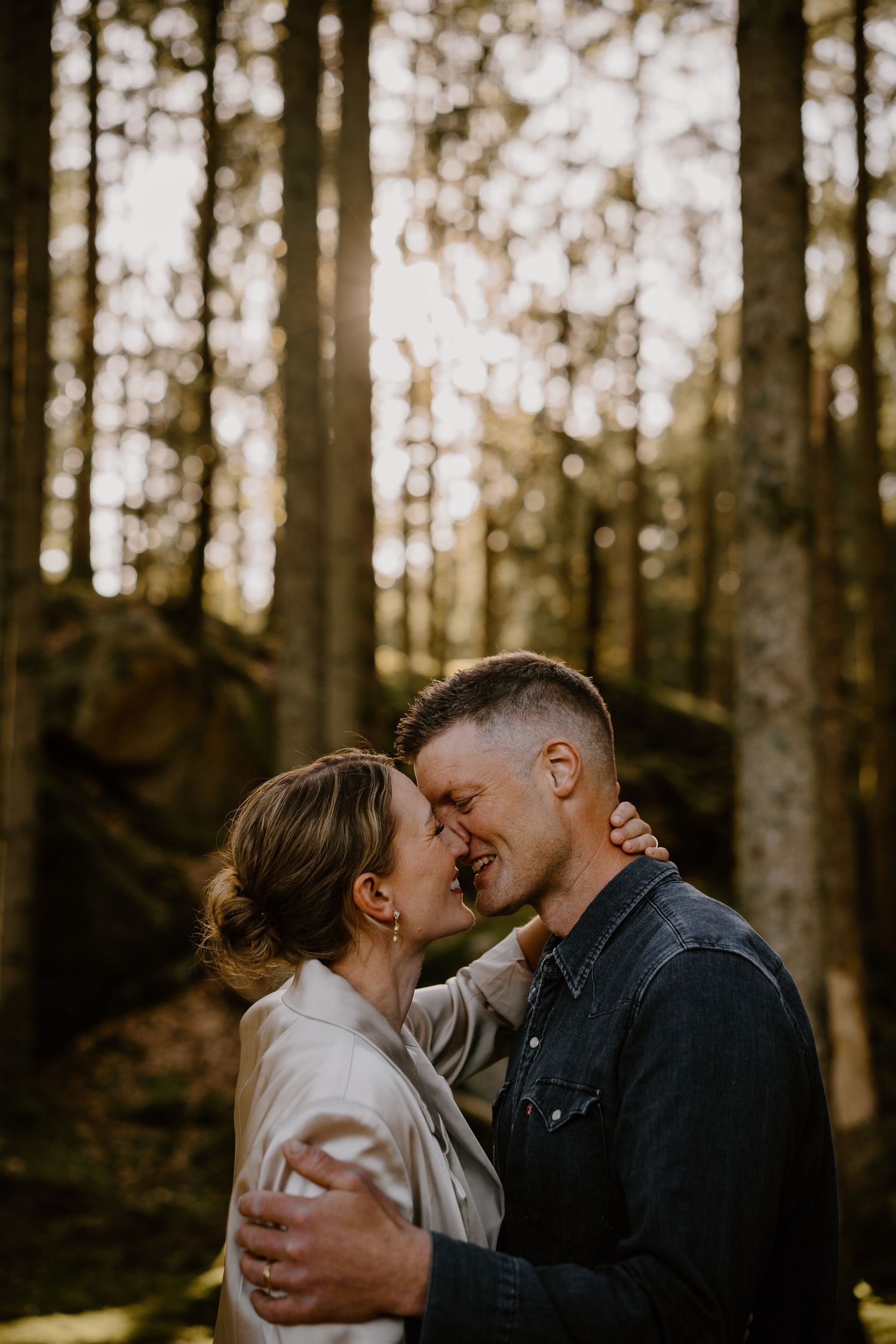 A couple shares an intimate moment while embracing in a sunlit forest setting.