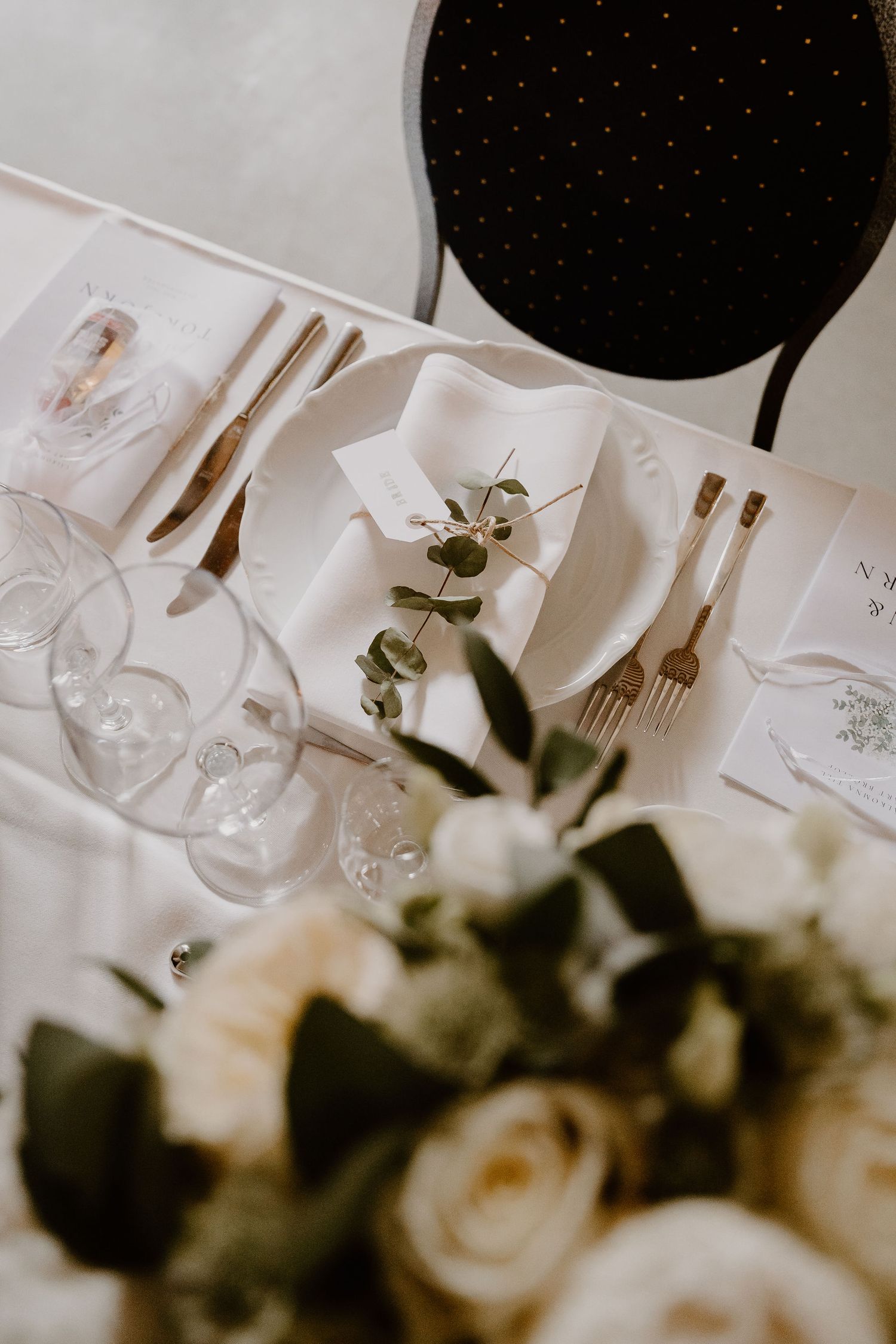 Elegant wedding reception table setting with white floral centerpiece, wine glasses, and black balloon decor overhead.