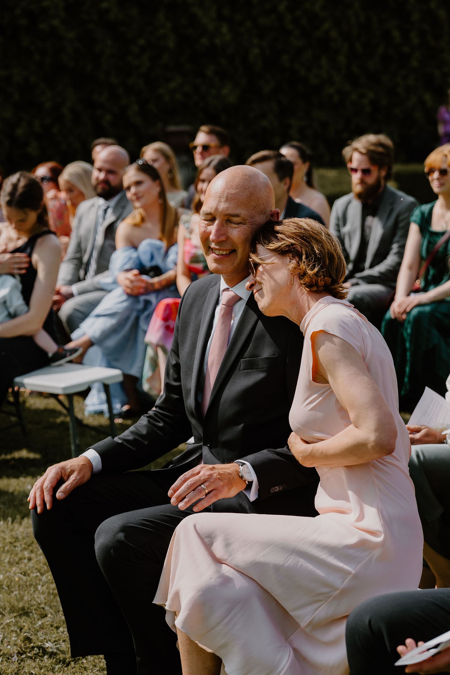 An intimate outdoor wedding ceremony with guests seated on chairs in a sunny garden setting.