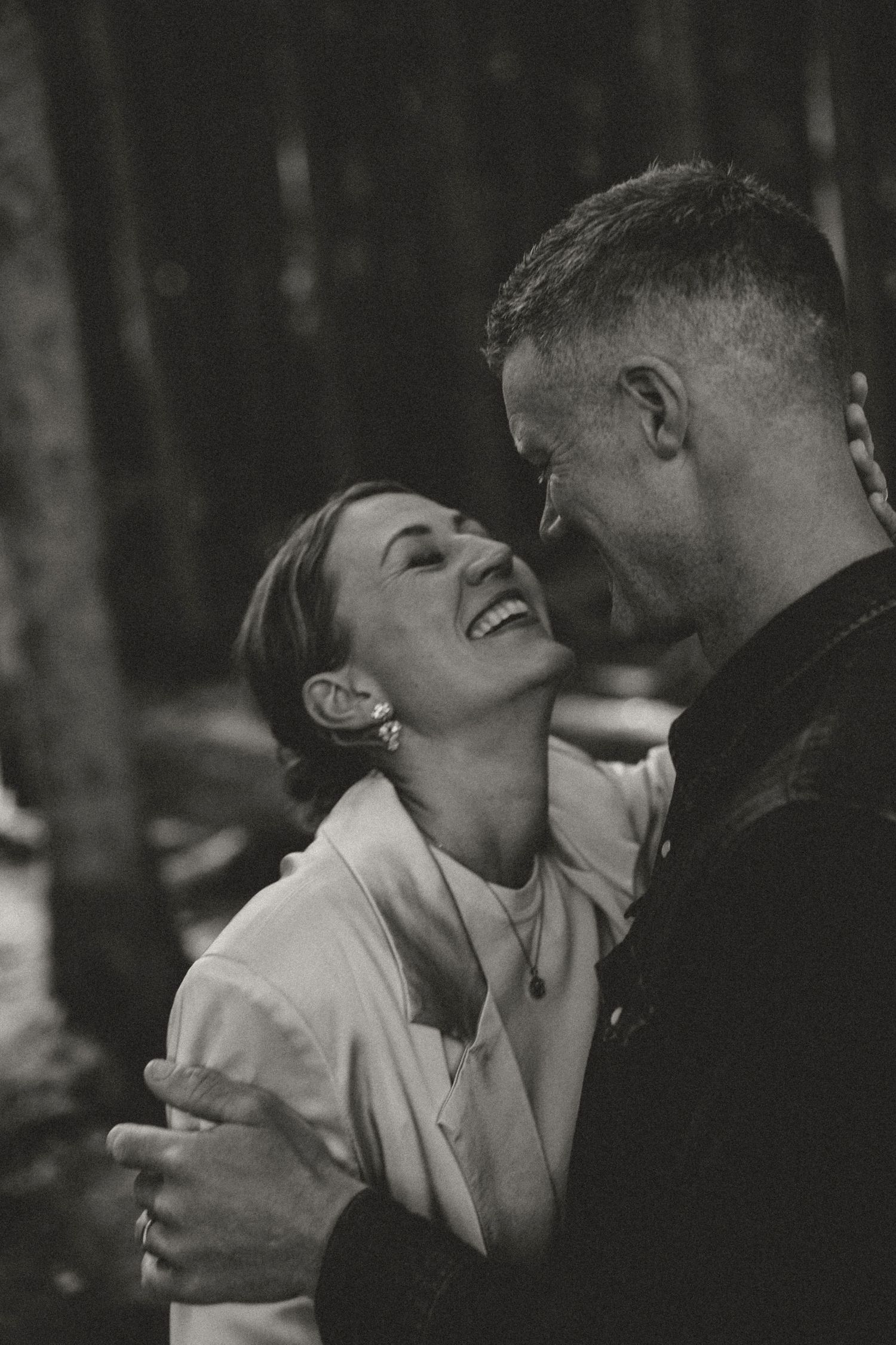 Black and white portrait of a romantic couple sharing a joyful, intimate moment while embracing outdoors.