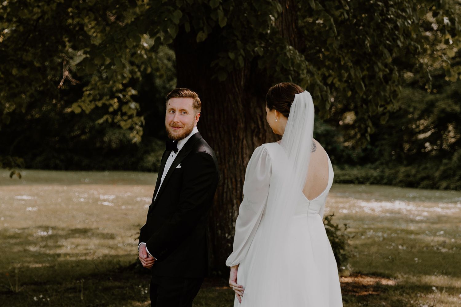 A groom glances over his shoulder during a first look moment with his bride in a garden setting.