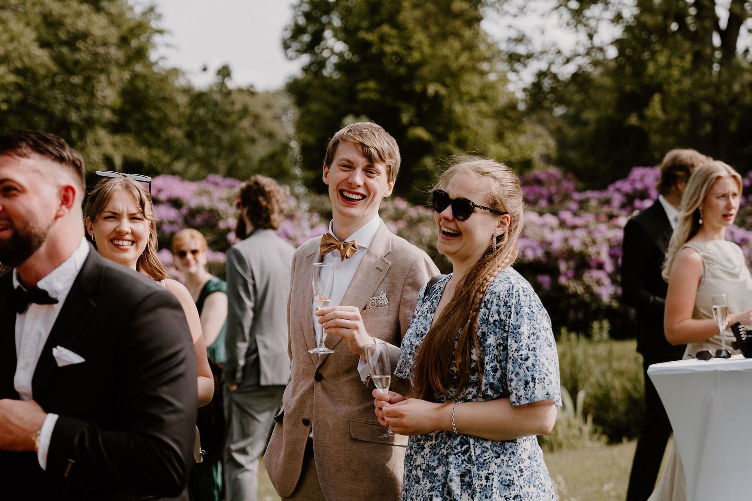 Wedding guests mingle and socialize during an outdoor cocktail hour reception beneath blooming trees.