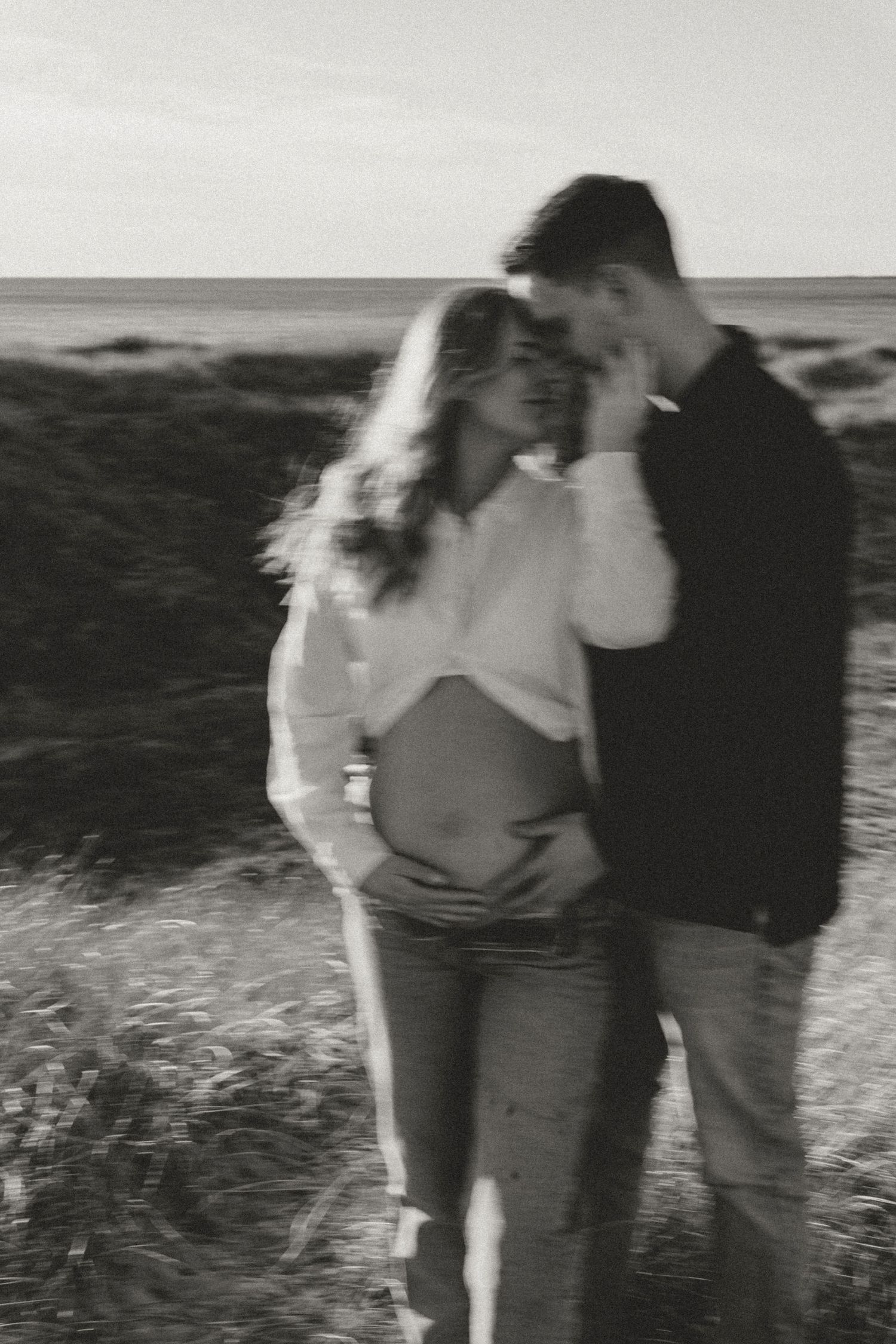 A romantic black and white photo captures an intimate moment between a couple on a coastal hillside.